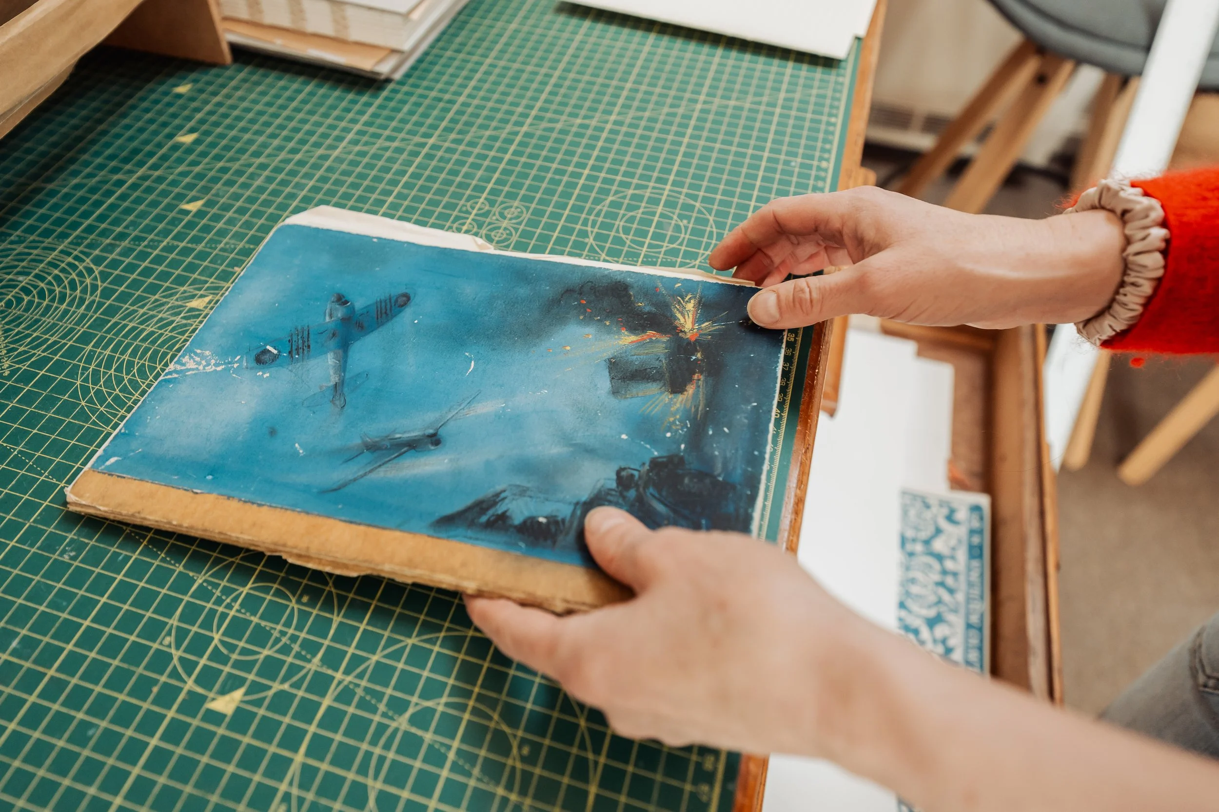 Close-up of a person holding a vintage science fiction paperback book with a blue cover, on a green cutting mat on a wooden table.
