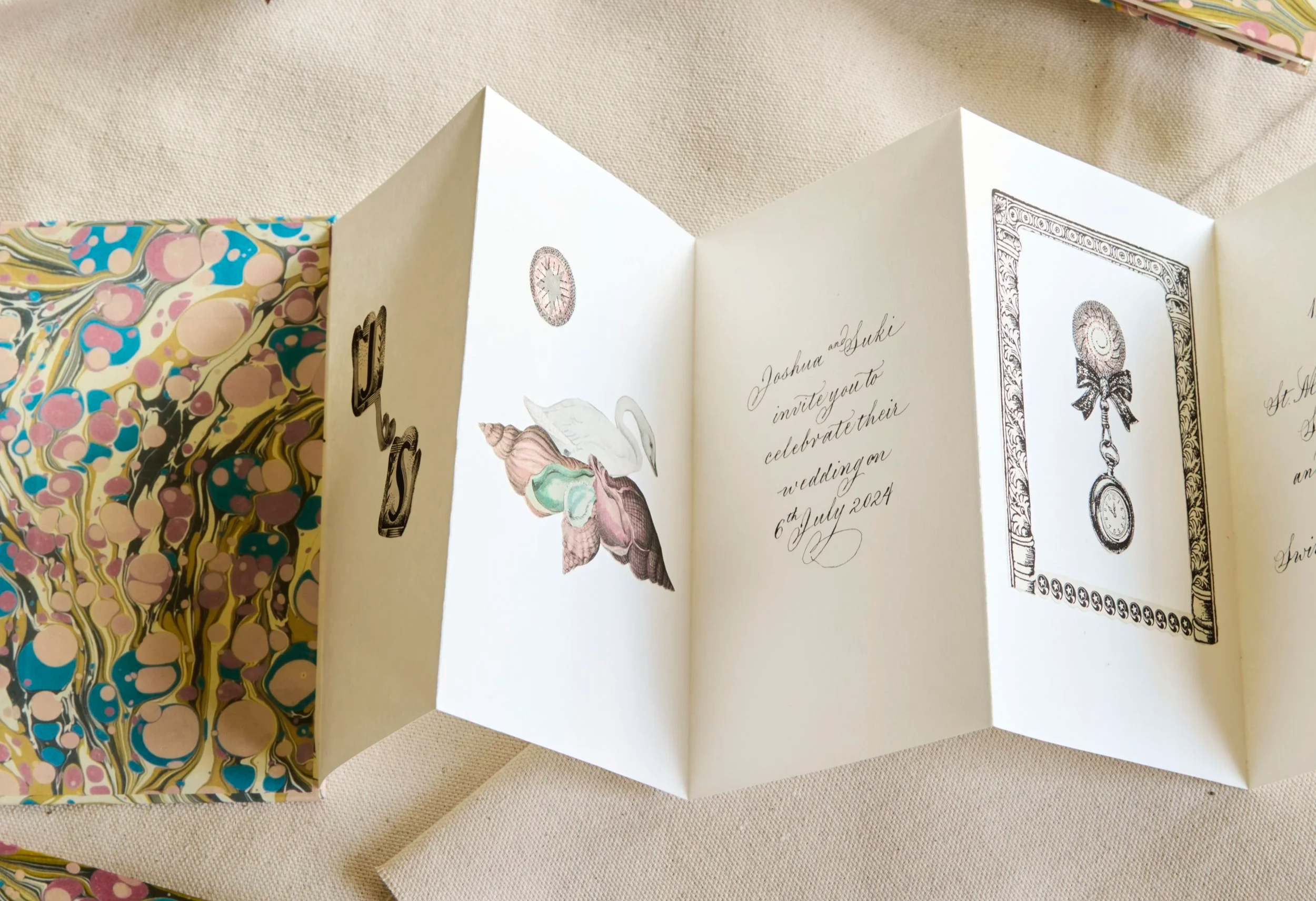 Open greeting card with wedding invitation inside, decorated with illustrations of seashells, a clock, and ornate frame designs, on a beige surface, with a patterned gift box in the background.