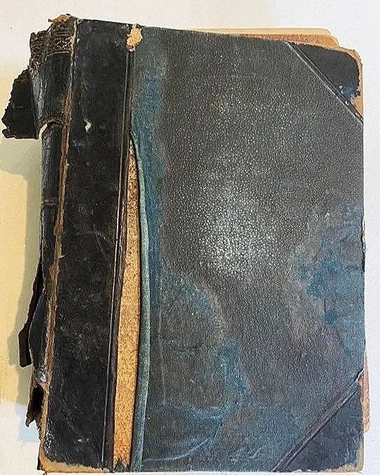 A torn and worn-out old black hardcover book with damage on the spine and edges.