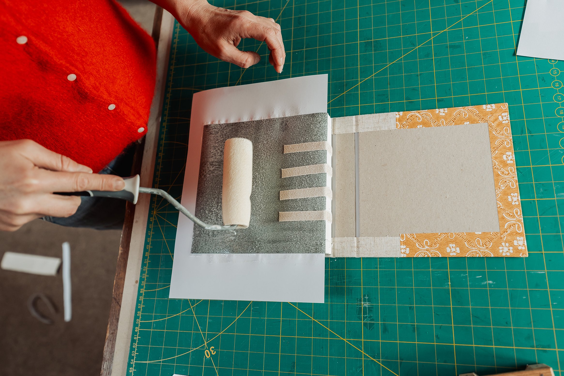 Person using a paint roller to cover a fabric with adhesive on a work table with a green cutting mat.