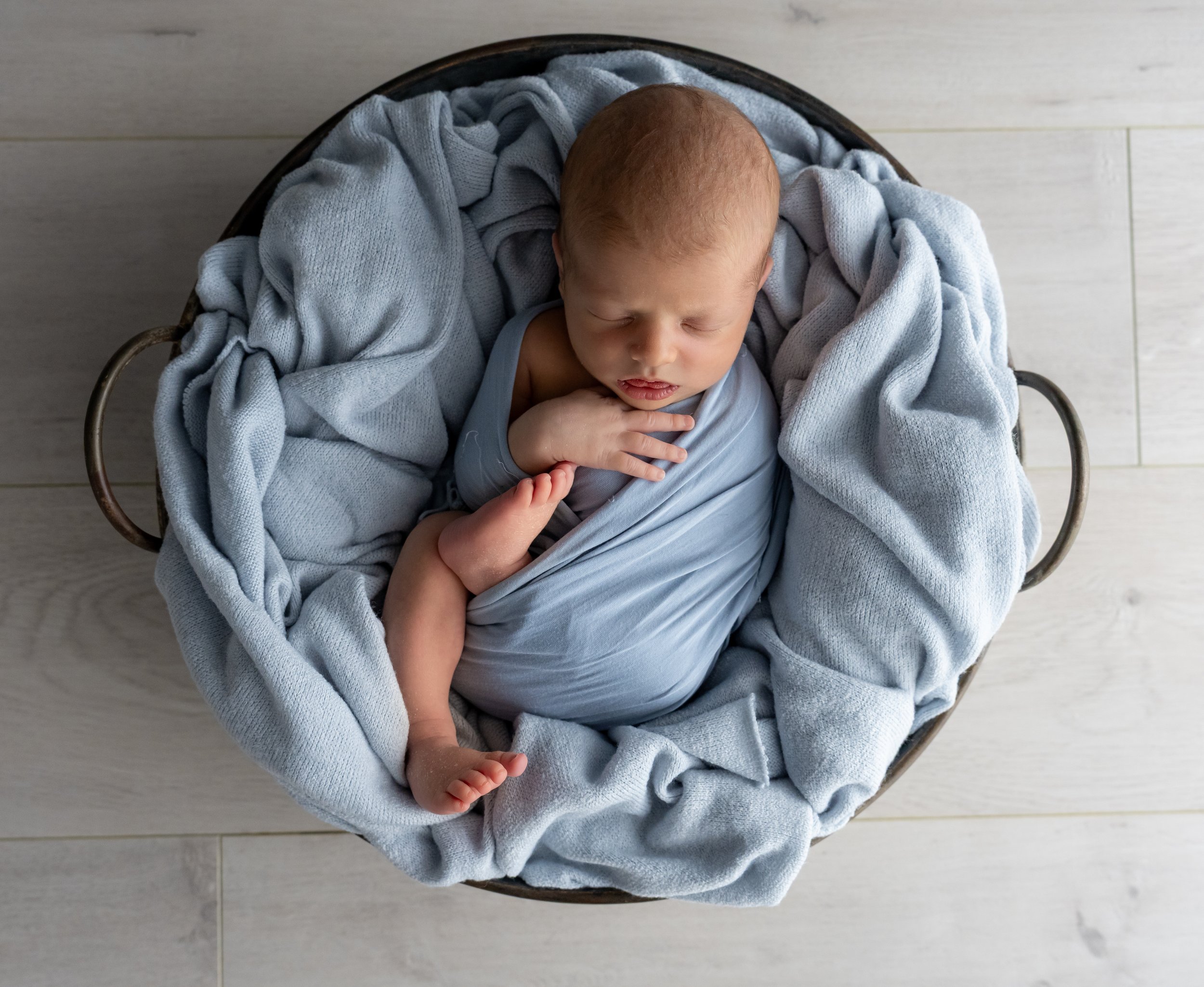Newborn baby sleeping in a woven basket wrapped in soft blue blankets.