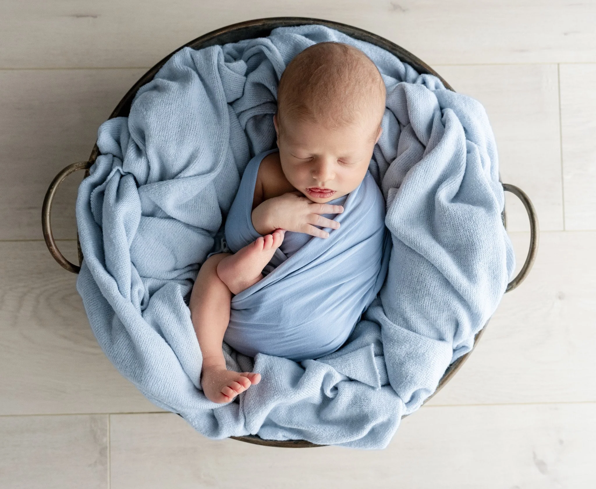 Newborn baby sleeping in a woven basket with soft blue blankets.