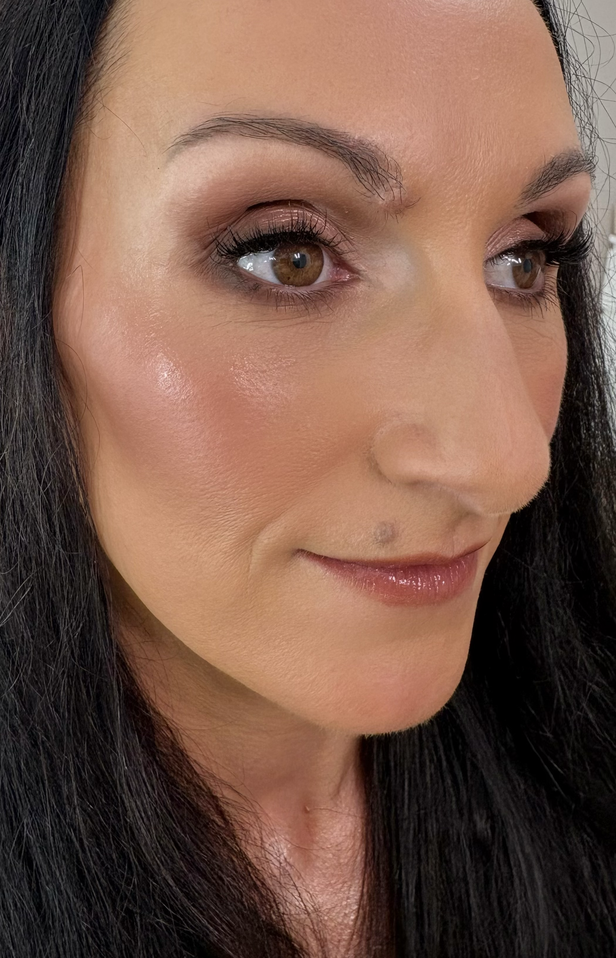 Close-up of a woman's face showing her brown eyes, well-defined eyebrows, long eyelashes, smooth skin with a subtle glow, and long black hair.