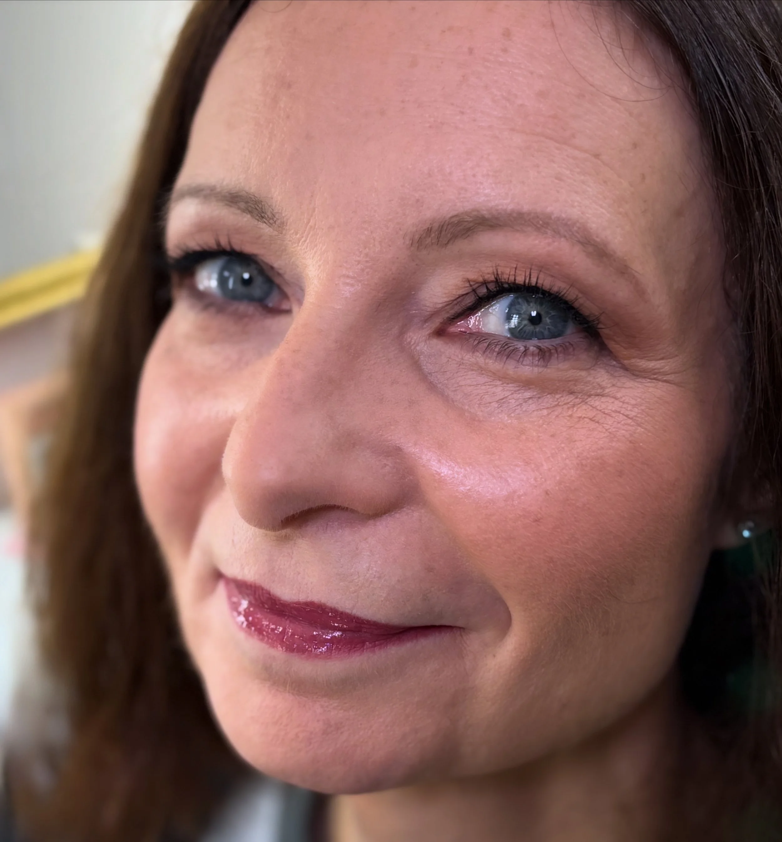 Close-up of a woman's face showing her blue eyes, forehead, and lips with pink lipstick. She has brown hair.