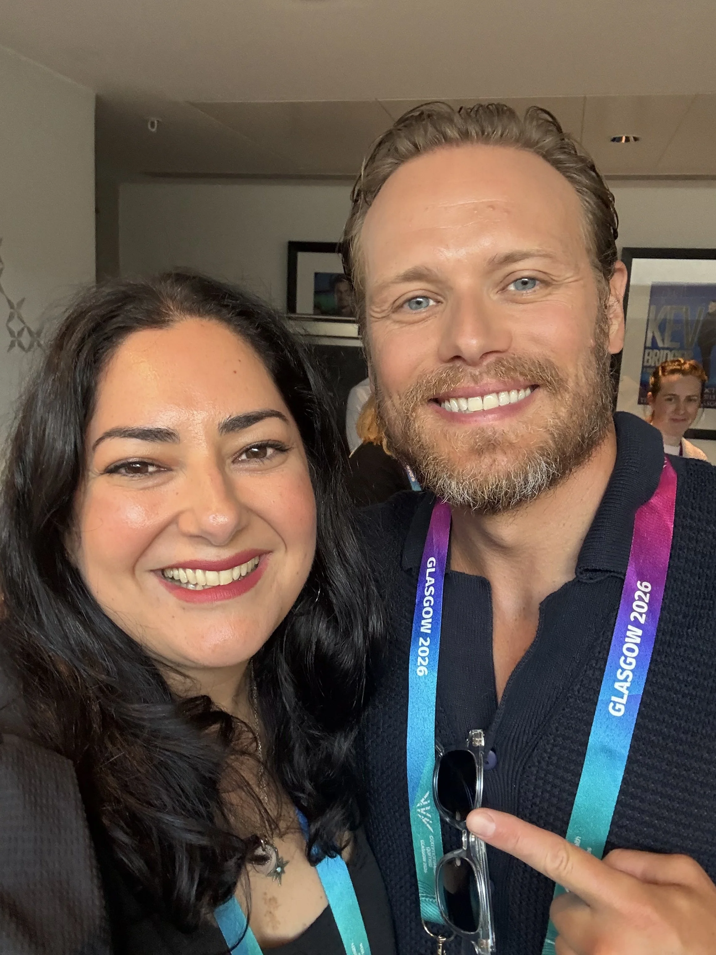 A smiling woman with dark hair and a man with a beard and light hair, both wearing conference badges that say Glasgow 2026, posing for a photo at an indoor event.