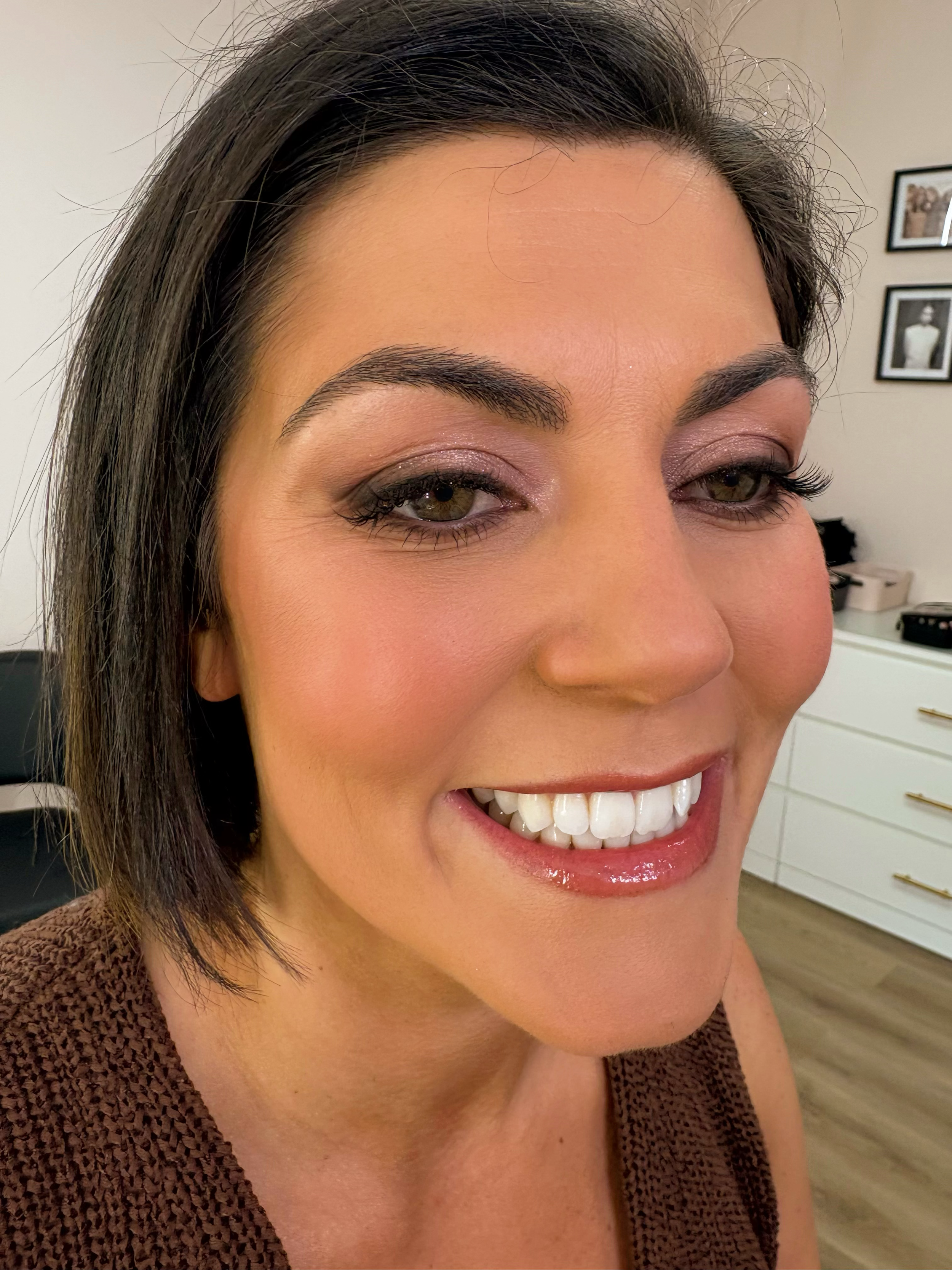 Close-up of a smiling woman with short dark hair, makeup, and visible teeth.
