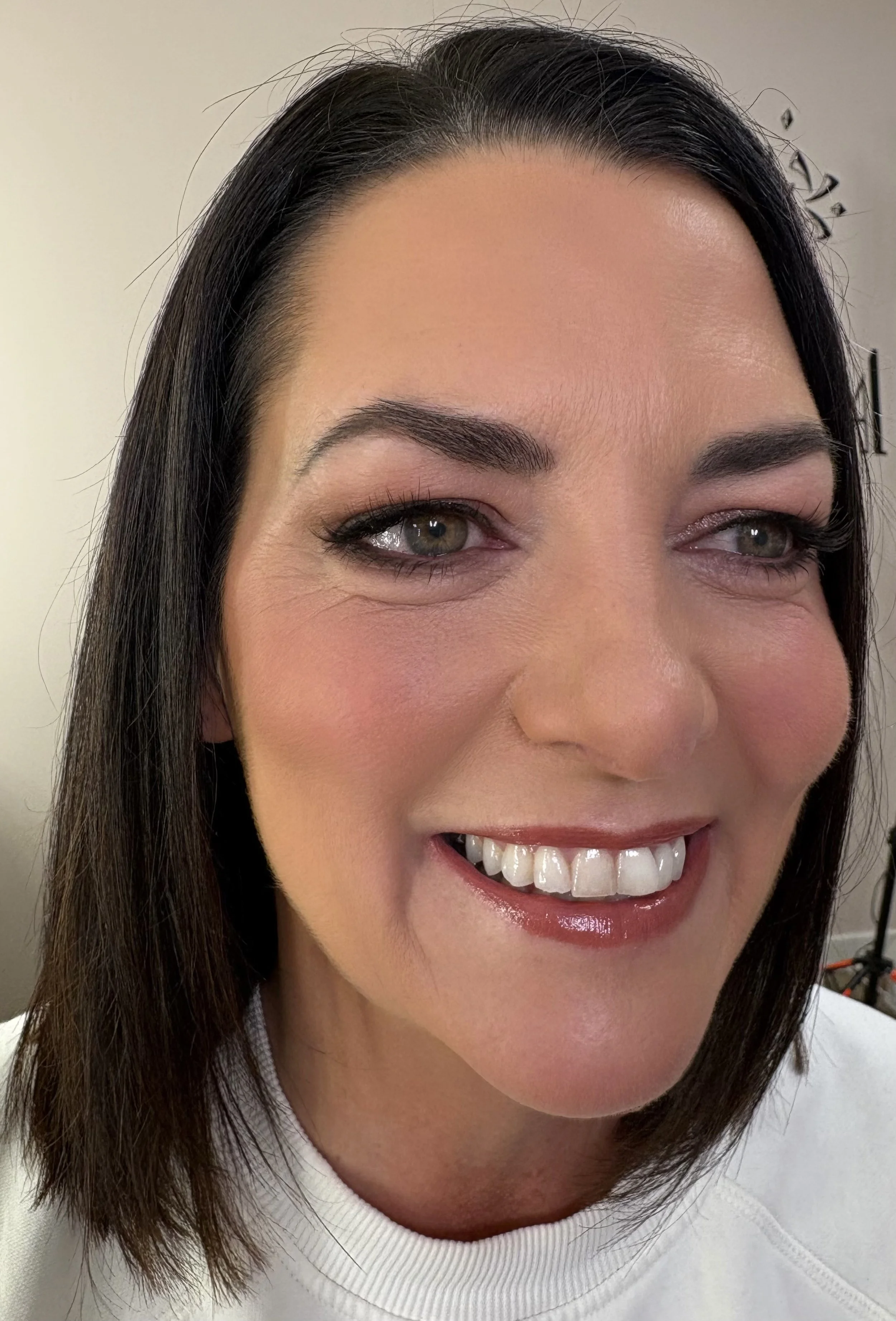 Close-up of a woman's face smiling, showing her teeth, with dark hair and makeup.
