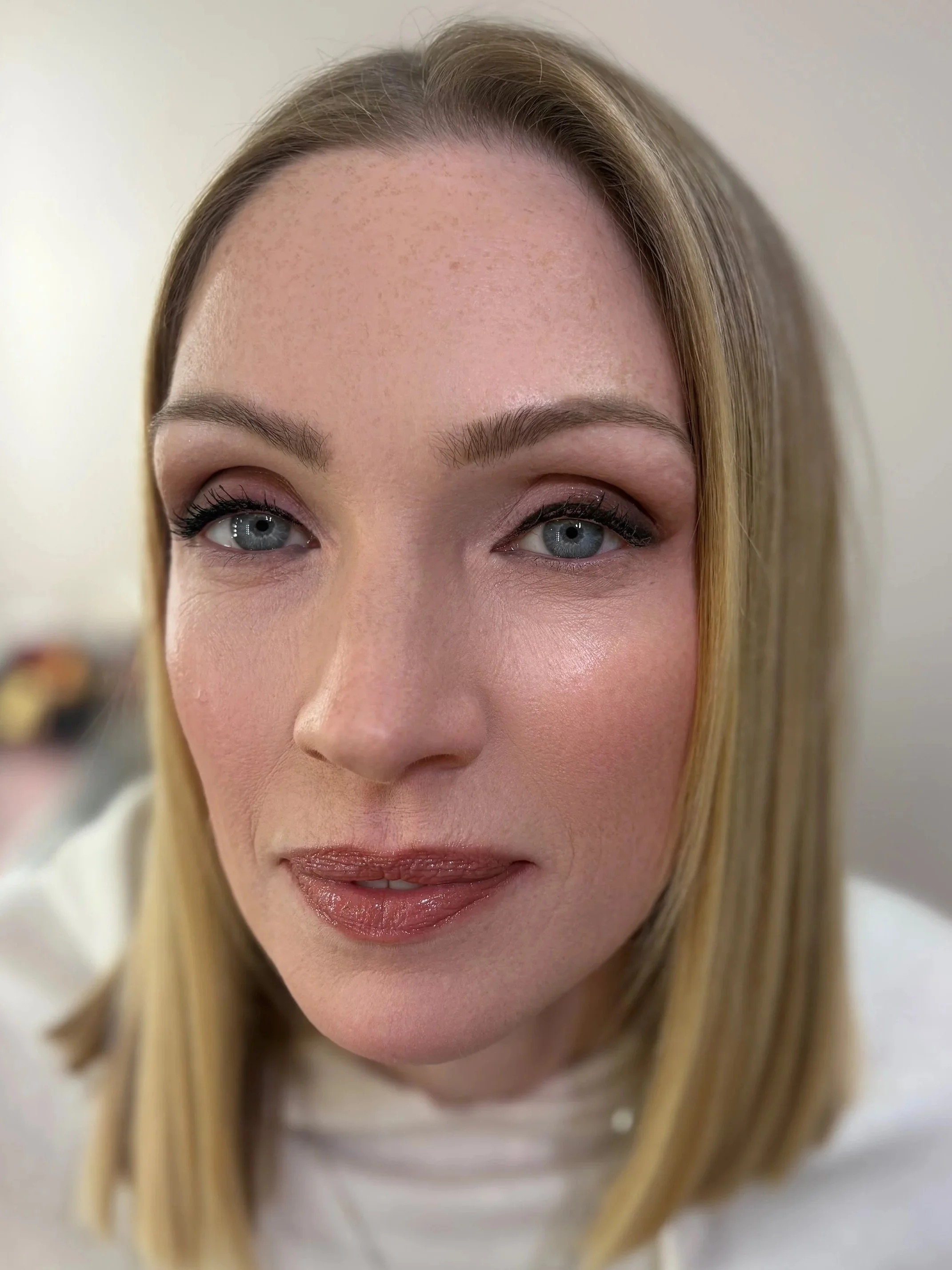 A woman's face with blonde hair, light skin, and blue eyes, smiling slightly, looking up and to the side.