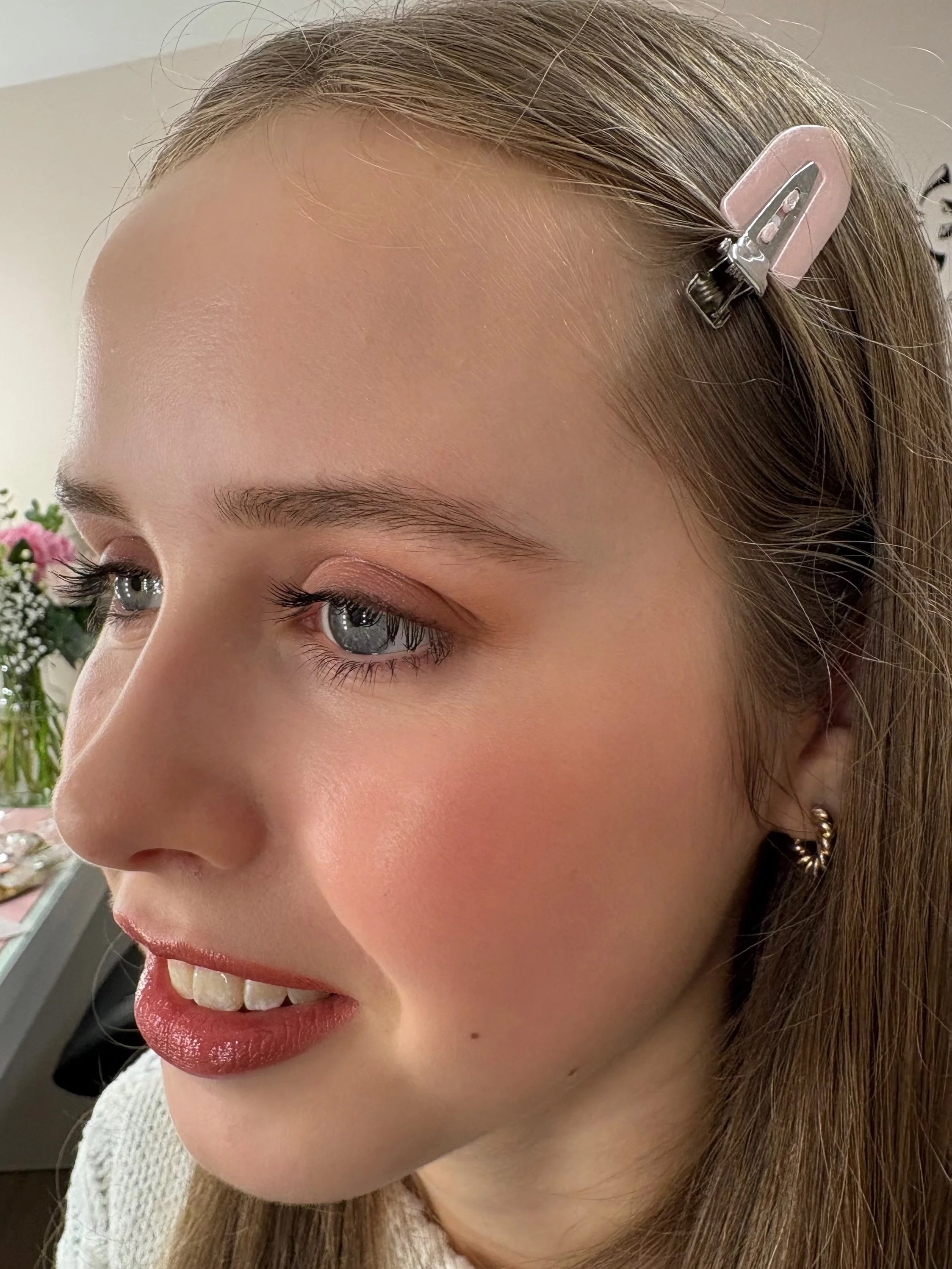 Close-up of a woman's face showing her eye, cheek, and side of mouth, with a pink hair clip in her brown hair.