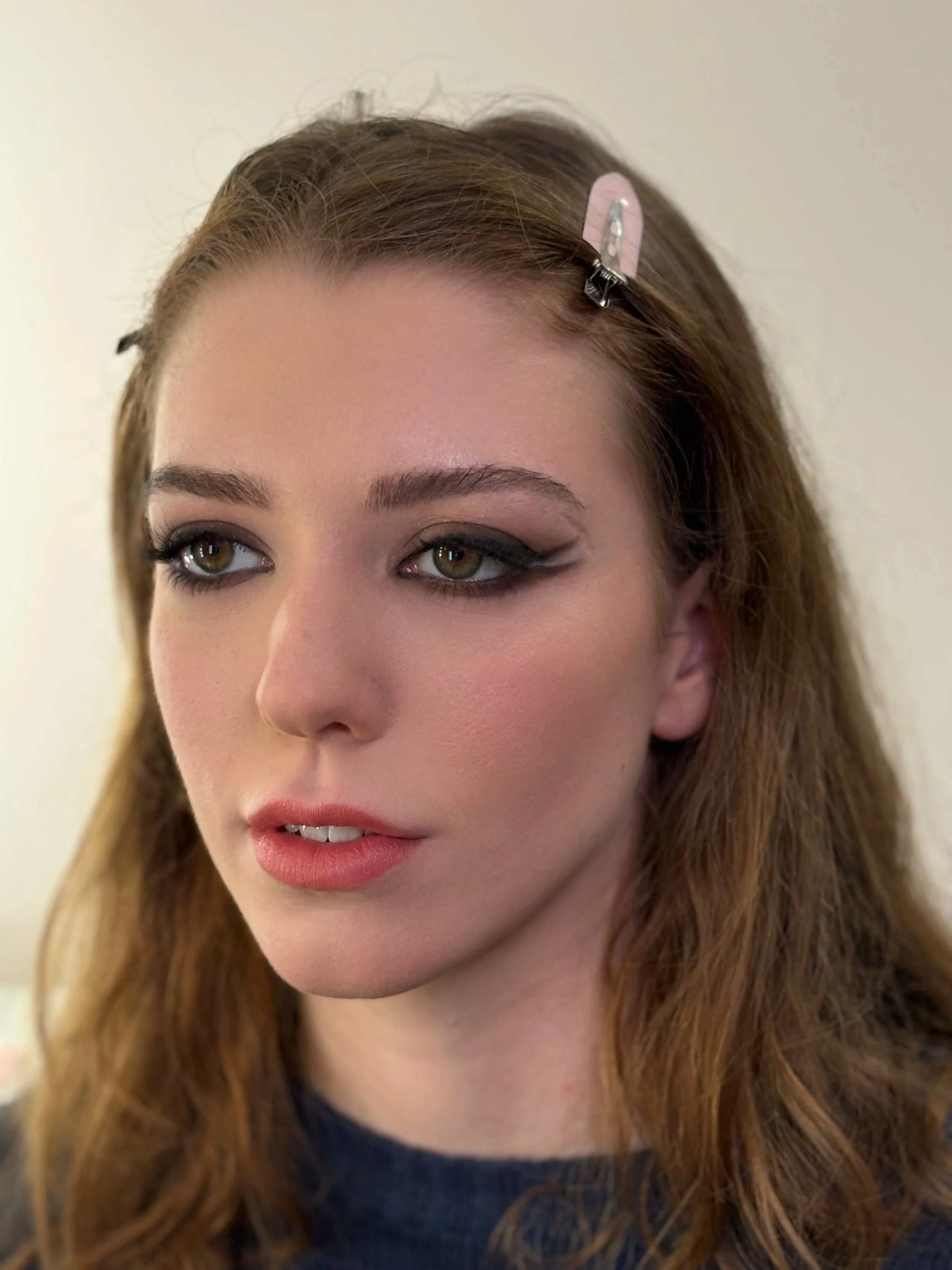 A woman with light skin, brown eyes, and long, wavy red hair, wearing makeup, with a hair clip in her hair.