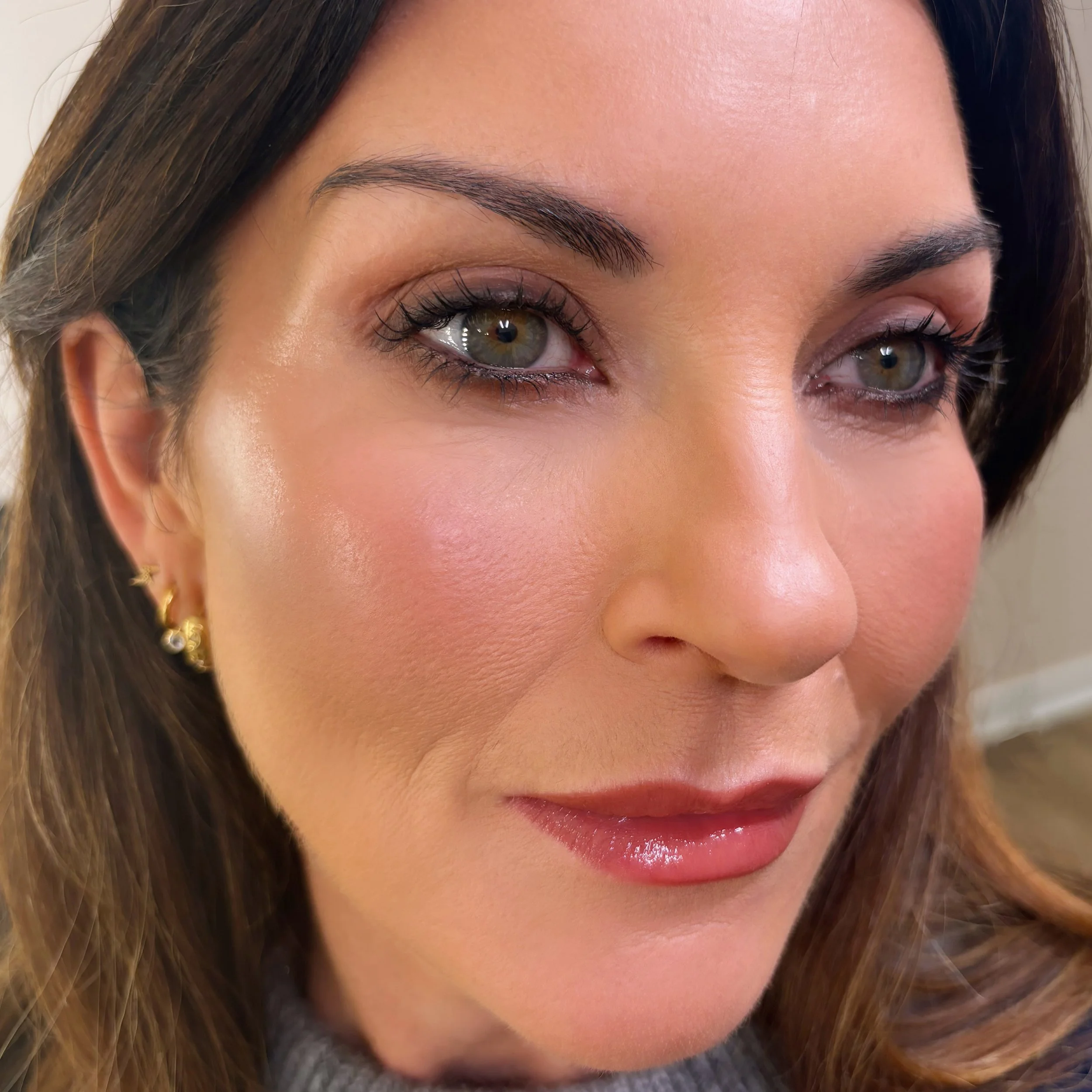 Close-up of a woman's face showing her right eye, eyebrows, and part of her lips with shiny lipstick, with long brown hair.