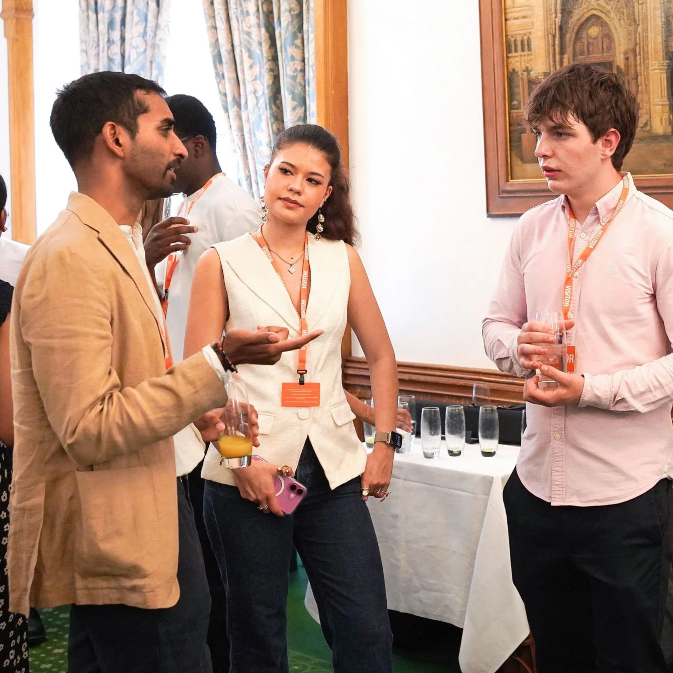 Four people having a conversation at a formal event, with water and juice glasses on a table in the background.