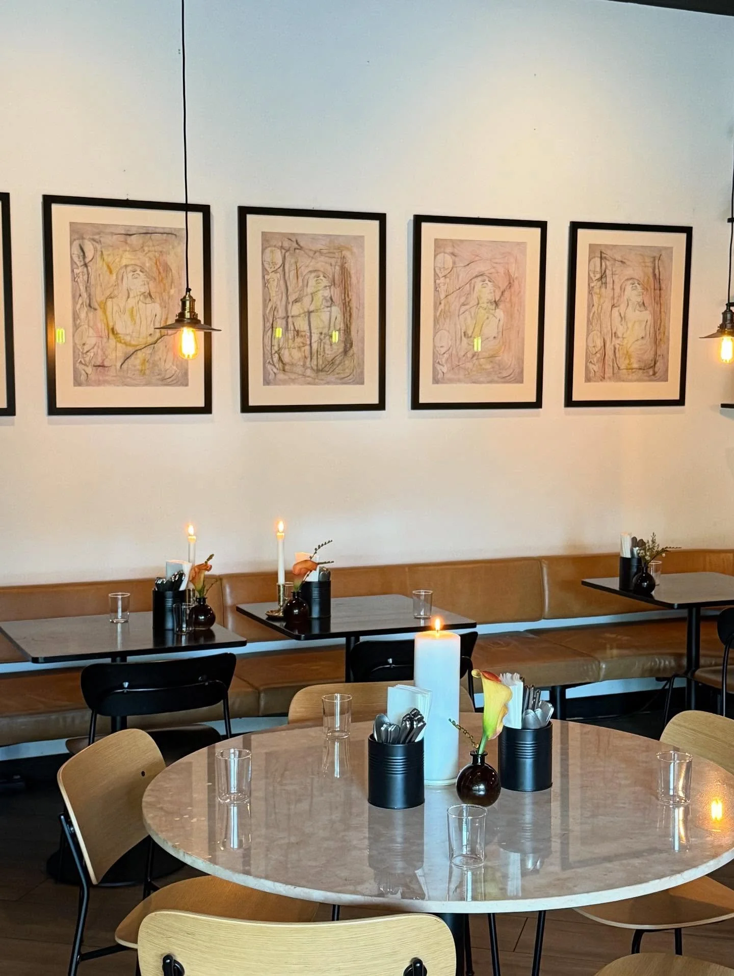 Innredning av en moderne kafé eller restaurant med bord, stoler, blomsterdekorasjoner, lysende lamper og kunst på veggen.