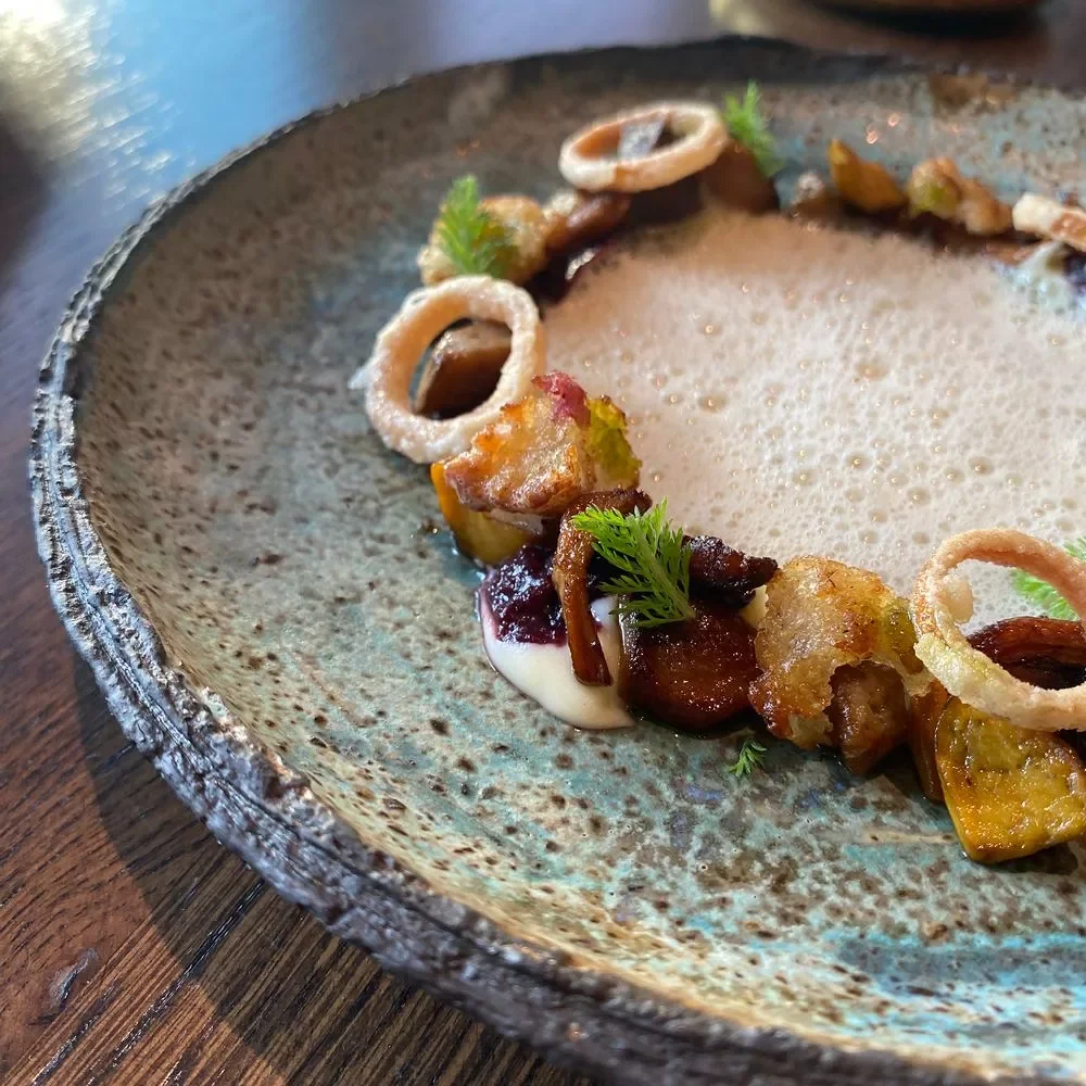 En tallerken med dekorative retter som inkluderer sopp, urter og fet saus.