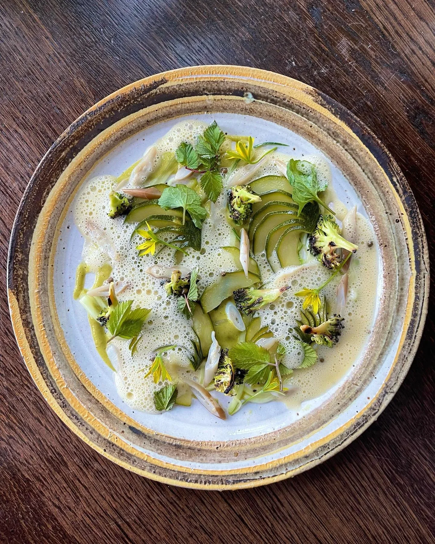 En tallerken med en cremeaktig suppe med grønnsaker og urter, servert i en keramisk skål på en treplate.