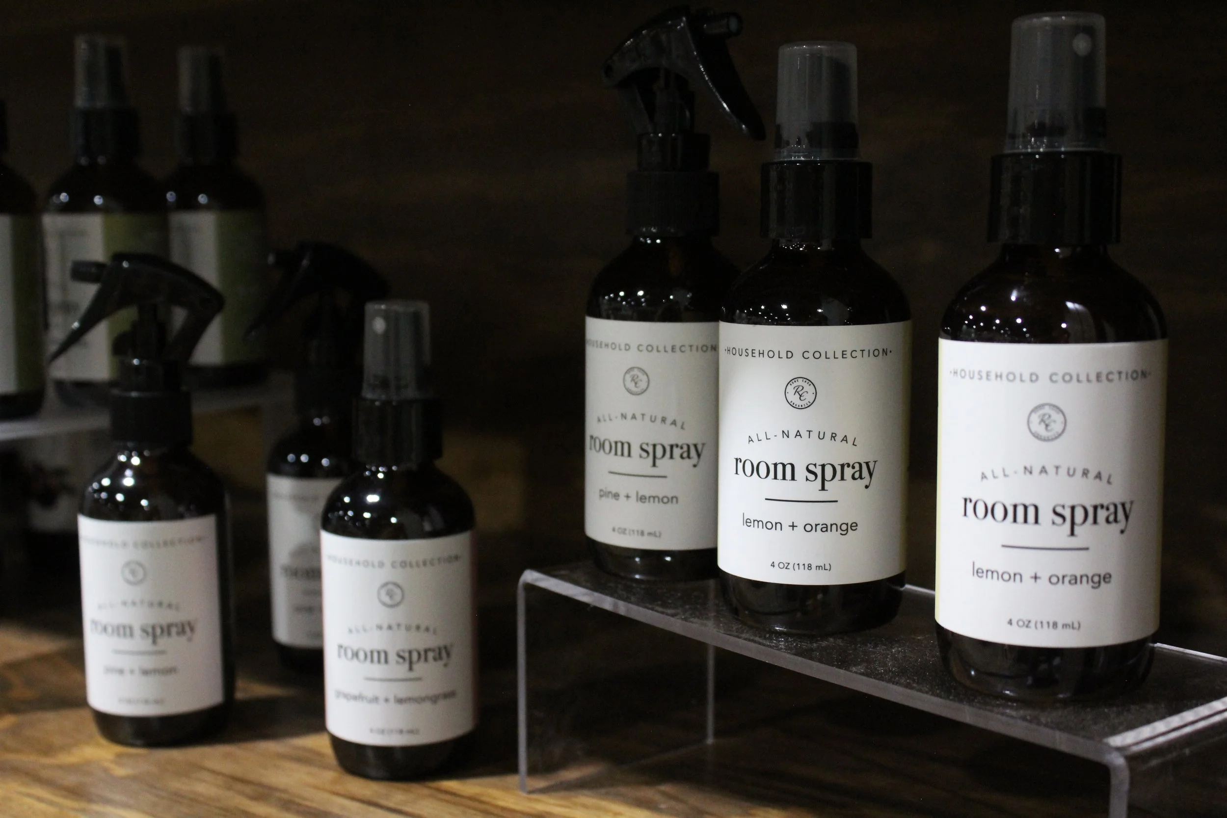 Multiple bottles of household all-natural room spray labeled lemon + orange, placed on a wooden shelf.
