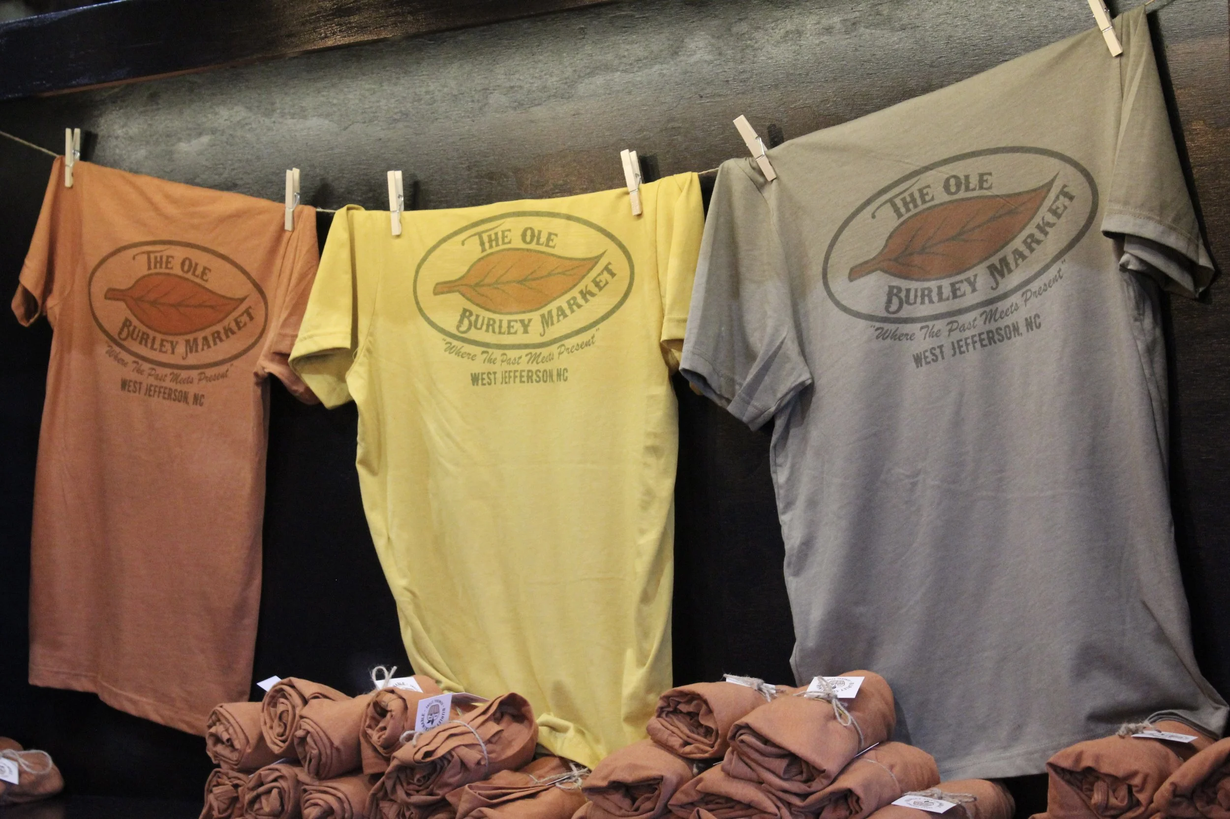 100 cotton, colorful T-shirts featuring the logo and text of The Ole Burley Market in West Jefferson, NC.