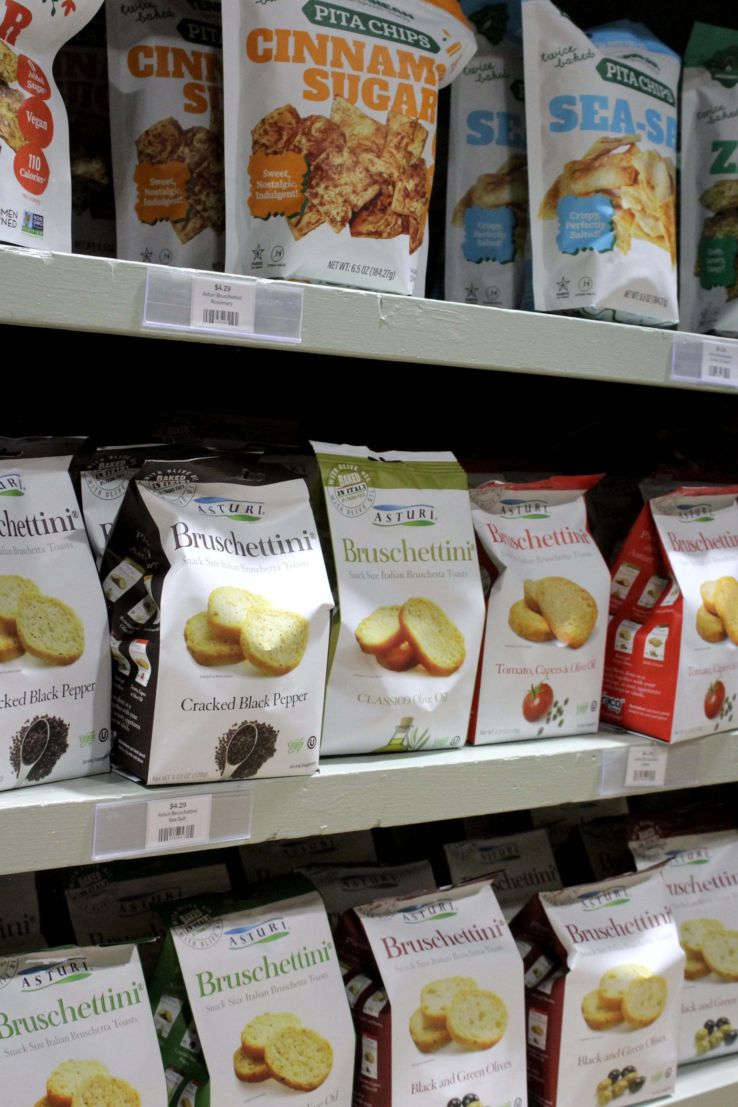 Shelf of various flavors of Asturi bruschettini snack toasts, including black pepper, classic olive oil, tomato with capers and olive oil, and black and green olives, at Burley Sustainable General Store in West Jefferson, NC.