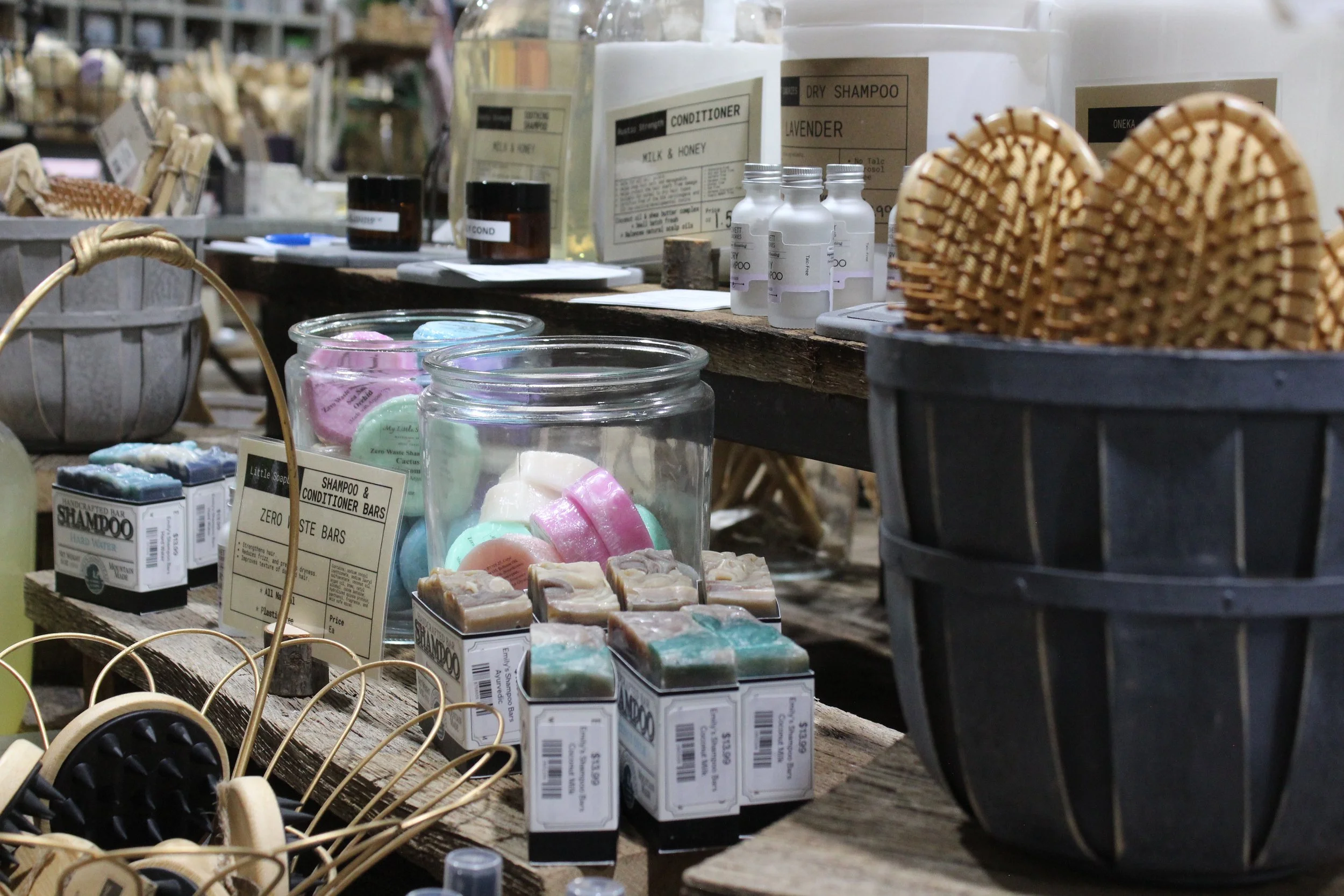 Display of natural soap products, bottles and jars, on rustic wooden shelves, with wicker baskets and soap bars at Burley Sustainable General Store in West Jefferson, NC.