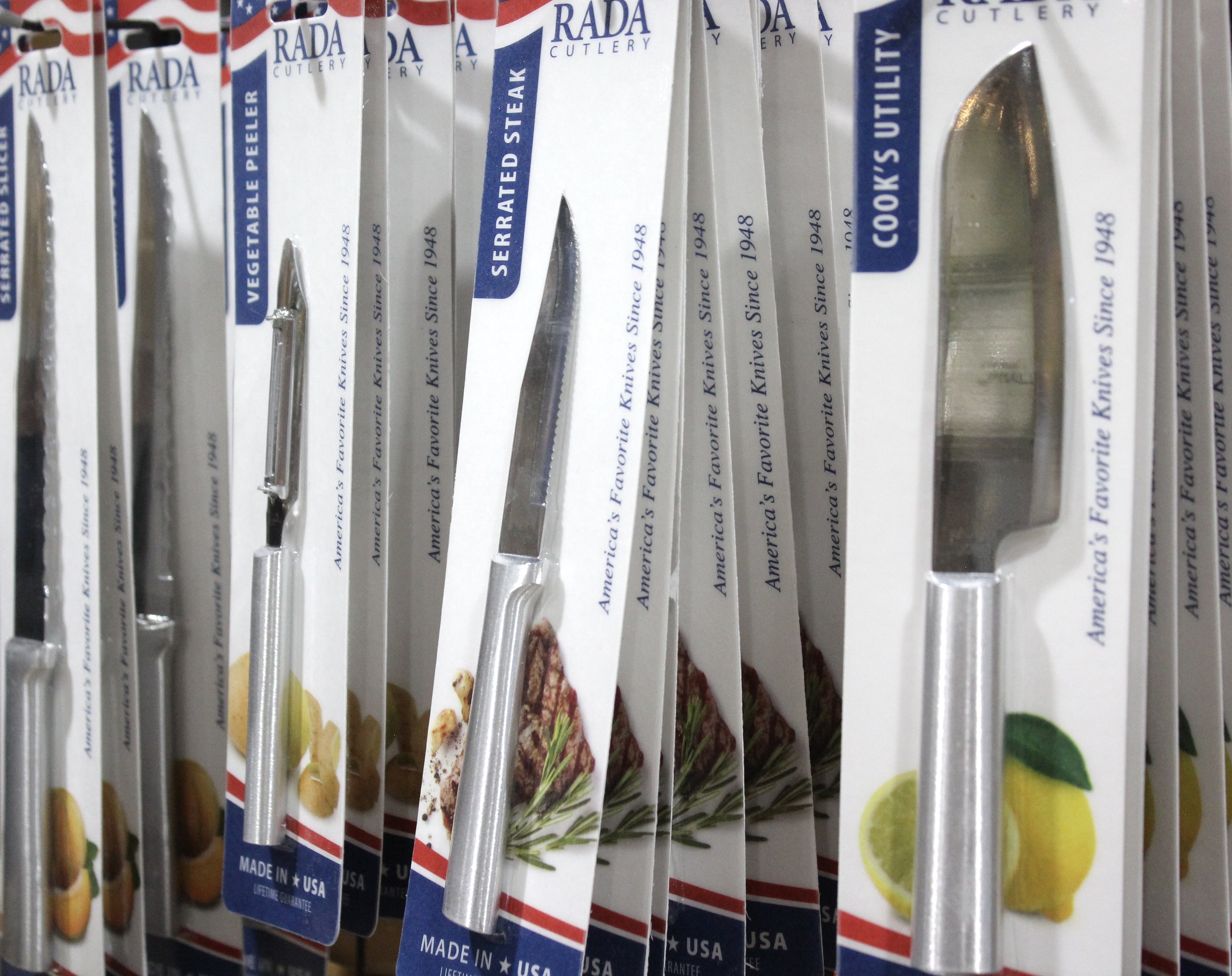 Multiple Rada Cutlery serrated steak knives in packaging on a store shelf, showing the packaging design with blue, made in the USA.