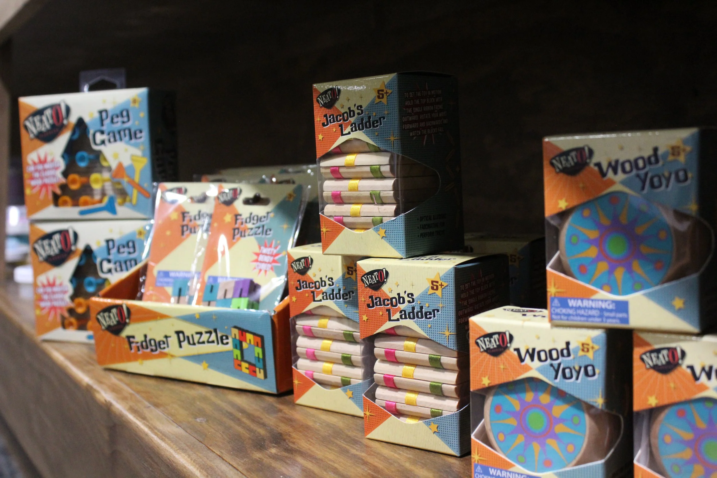 Colored boxed puzzles and toy sets on a store shelf, including Jacob's Ladder, Wood Yo Yo, and Peg Game.
