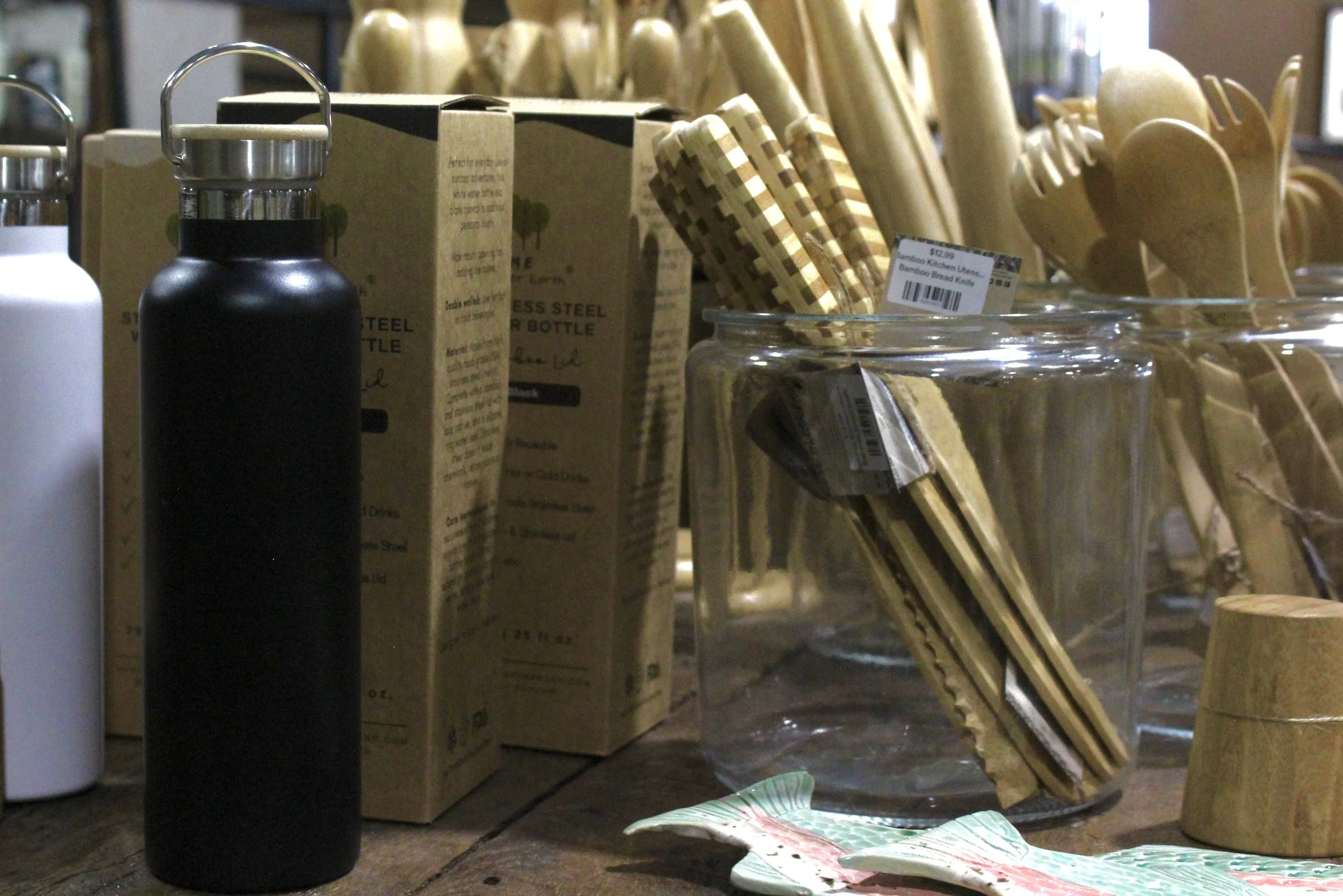 Assorted wooden kitchen utensils, including black and white bottles, bamboo kitchen utensils, and a clear glass jar, with a decorative leaf-shaped plate.
