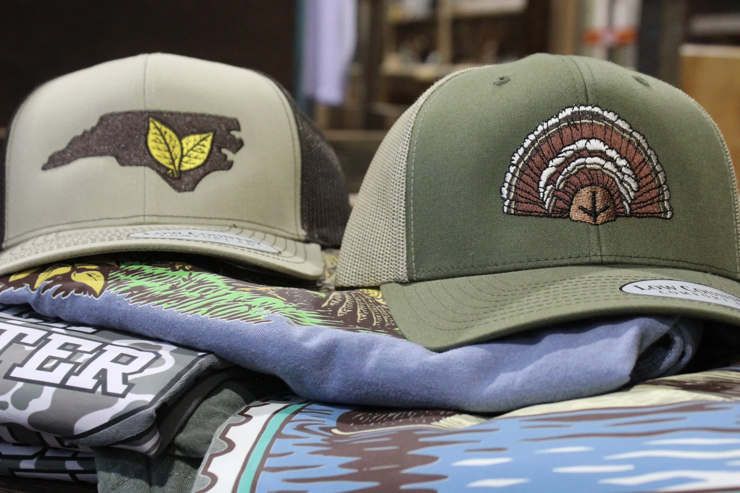 Two baseball caps, one with northcarolina leaf design, and the other with a turkey fan design, at Burley Sustainable General Store in West Jefferson, NC.