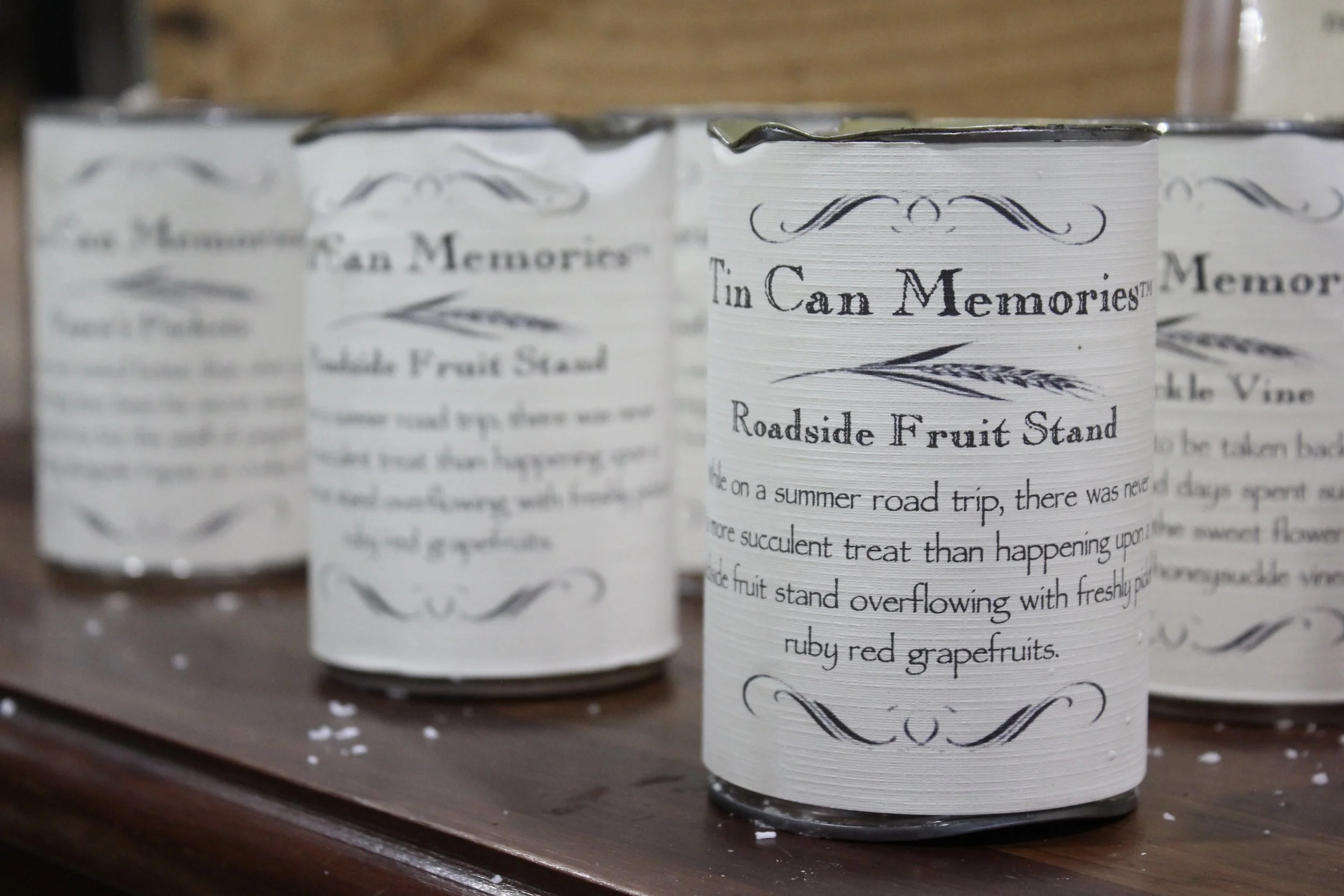Handmade natural candles in metal cans with vintage-style labels, reading 'Tin Can Memories' and 'Roadside Fruit Stand,' at Burley Sustainable General Store in West Jefferson, NC.