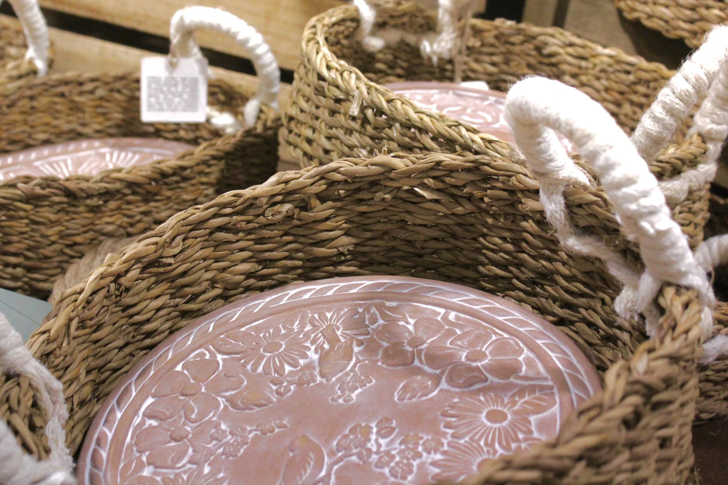 Woven wicker baskets with white rope handles, holding pink and white floral patterned plates for sourdough baking.
