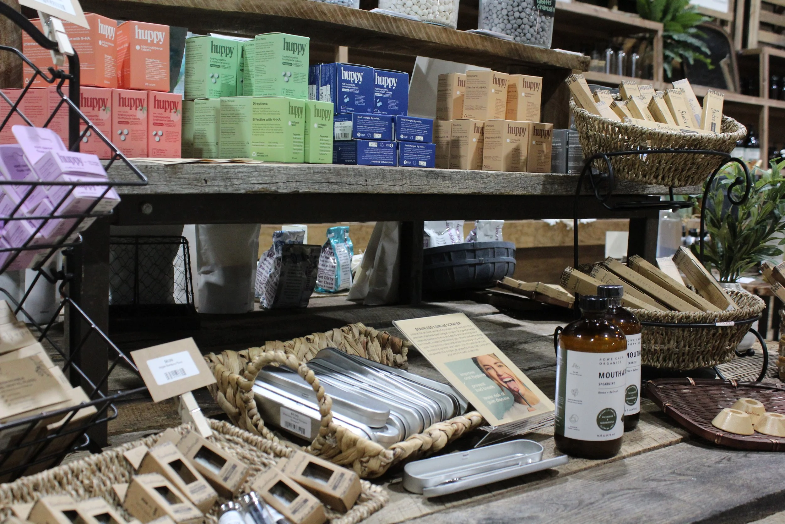 Display of various health and wellness products on wooden shelves, including herbal supplements, tablets, skincare items, and herbal powders, arranged in baskets and containers in a rustic store setting.