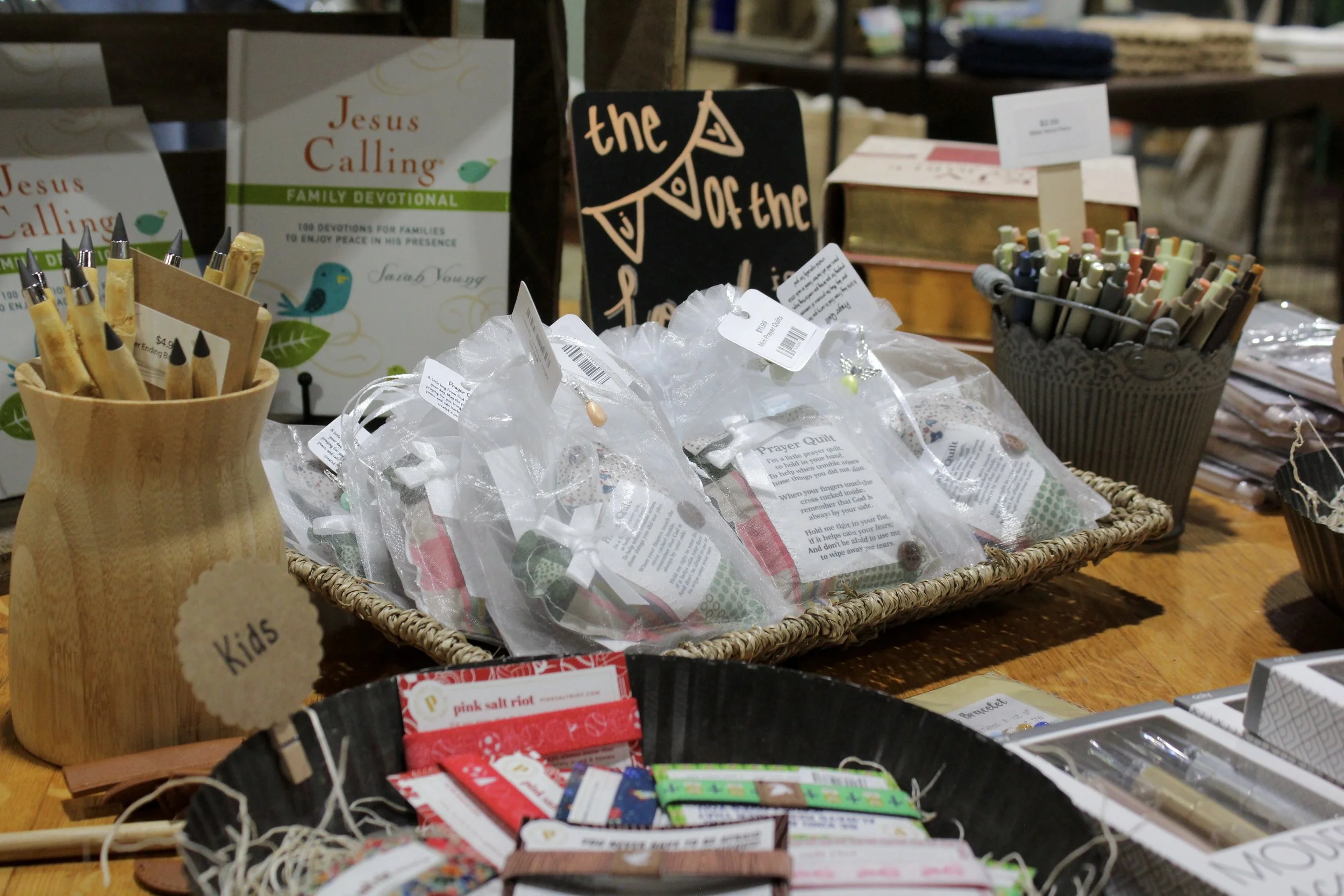 A display table with various Christian-themed items, including a booklet titled 'Jesus Calling' and a black chalkboard sign with the phrase 'the power of the Lord' written on it, surrounded by prayer cards, pens, and other small items.