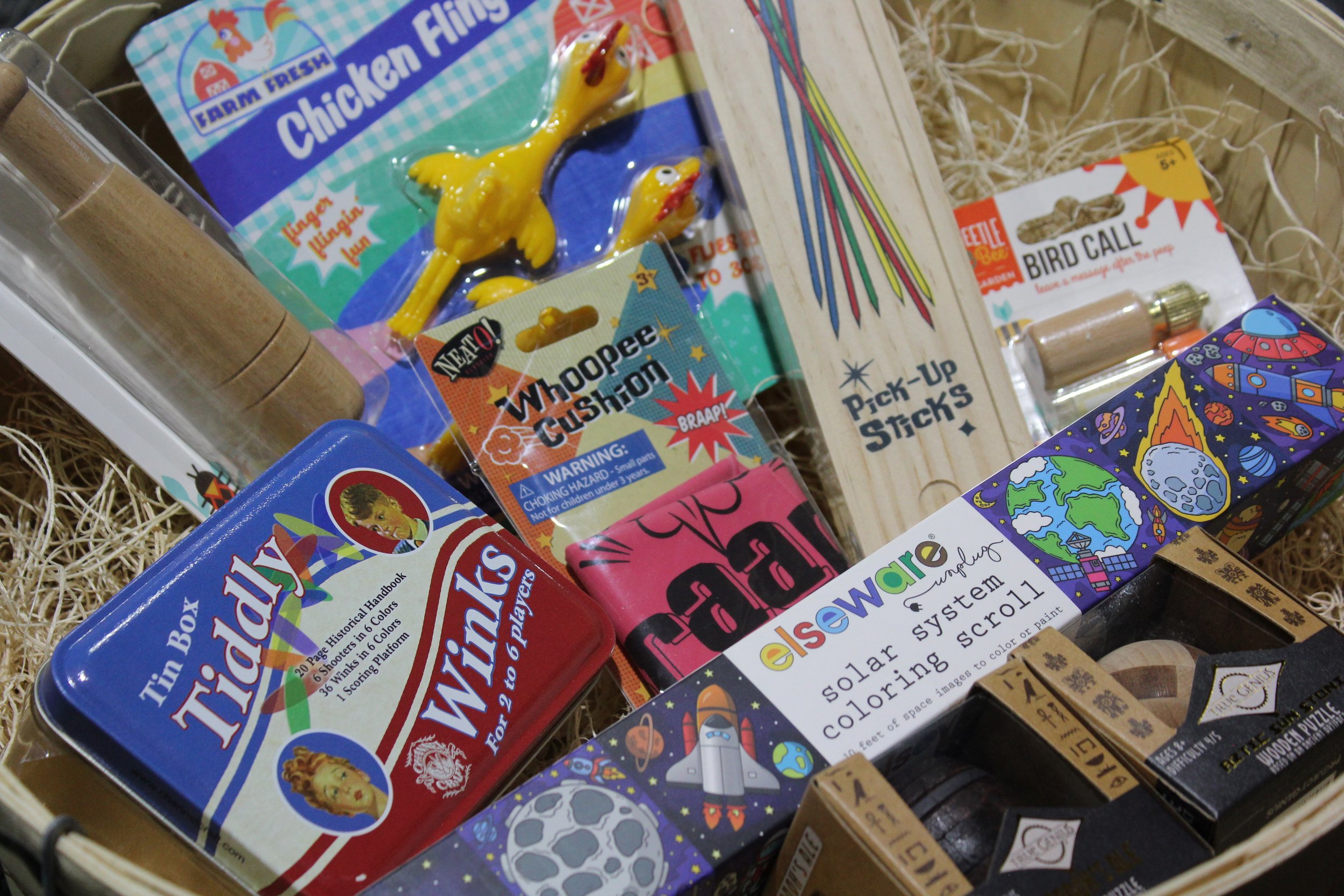A collection of toys and games, including a chicken flying game, a spaceship-themed coloring system, and a bird call toy, at Burley Sustainable General Store in West Jefferson, NC.
