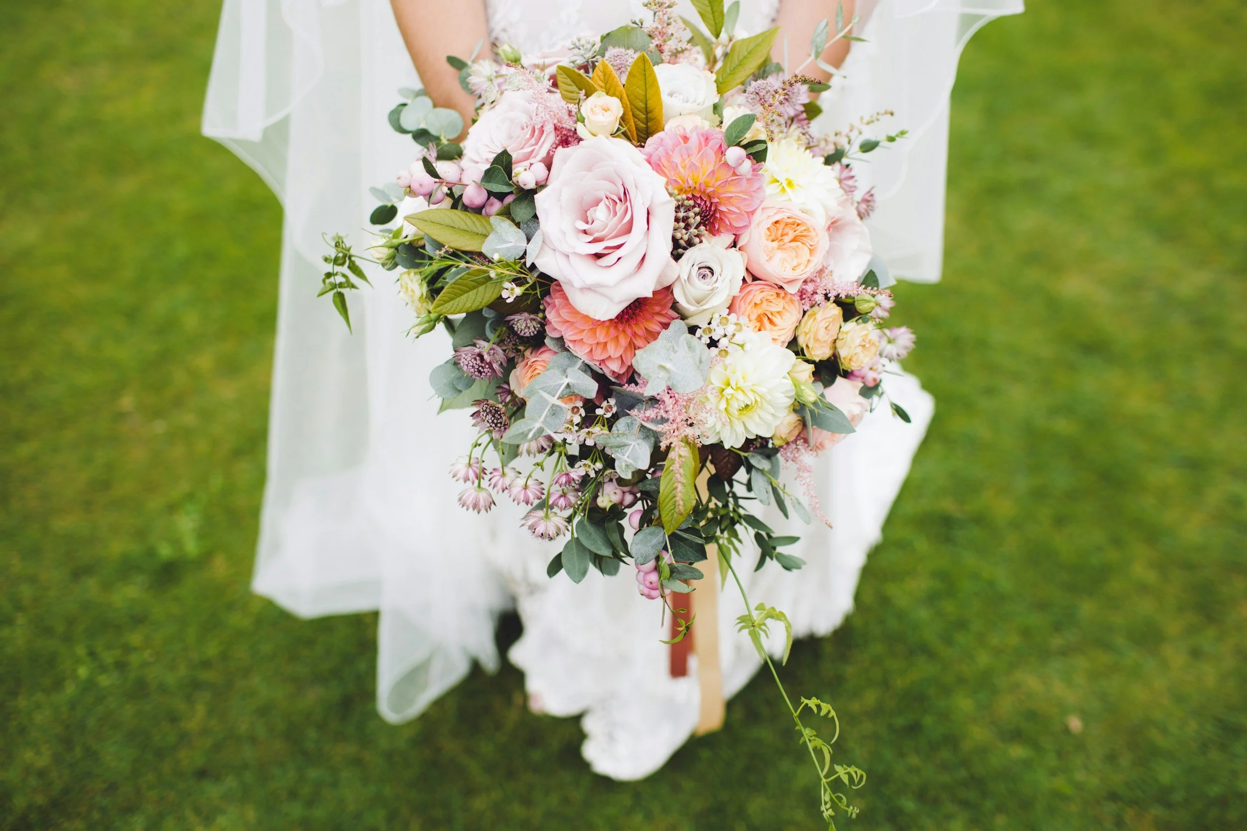 A person in a white dress holding a large, colorful bouquet of flowers outdoors on green grass.