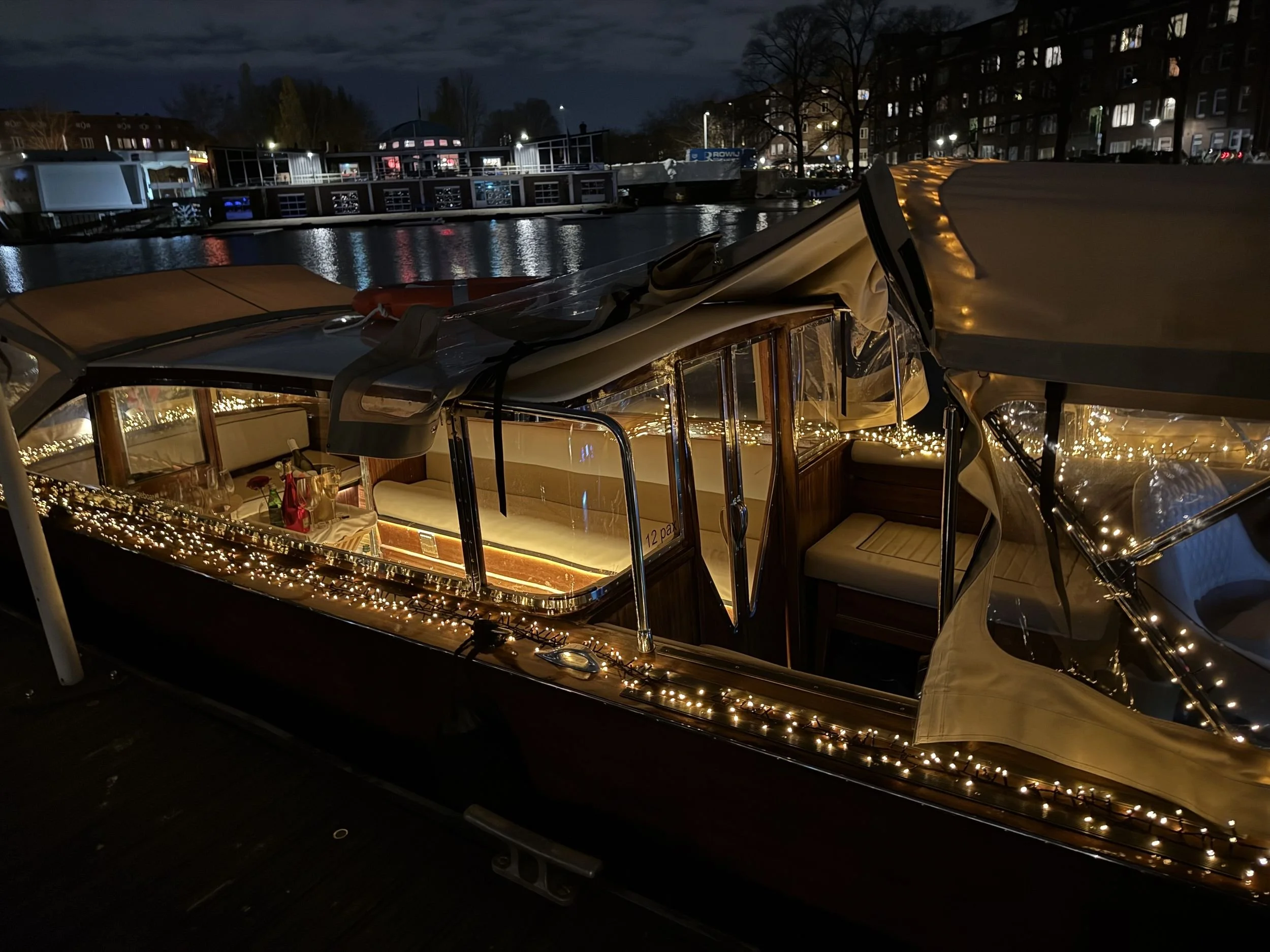 Private salon boat with warm lights moored on an Amsterdam canal at dusk