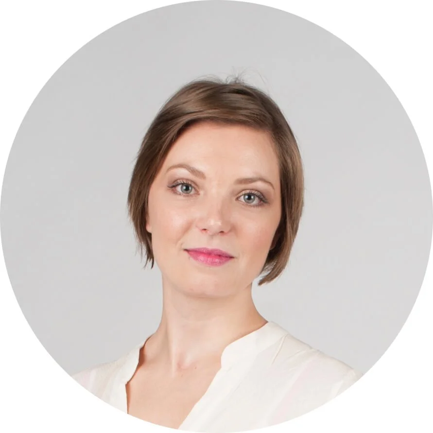 Portrait de l'architecte d'intérieur Sophie Durand avec des cheveux courts bruns, portant une chemise blanche, regardant l'appareil-photo dans un fond gris clair.
