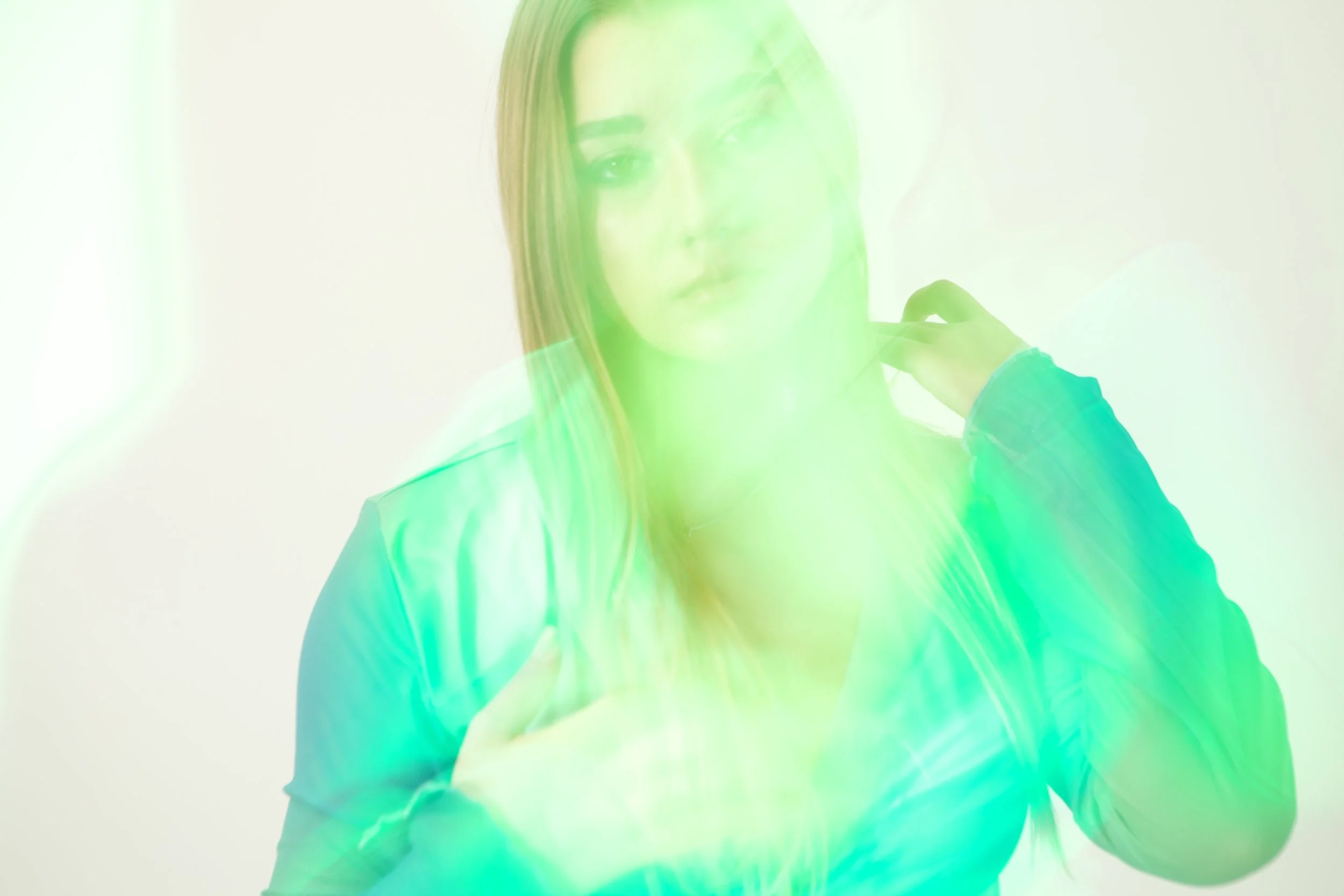 A woman with long hair is looking at the camera through a green-tinted glass or plastic surface, creating a distorted effect.