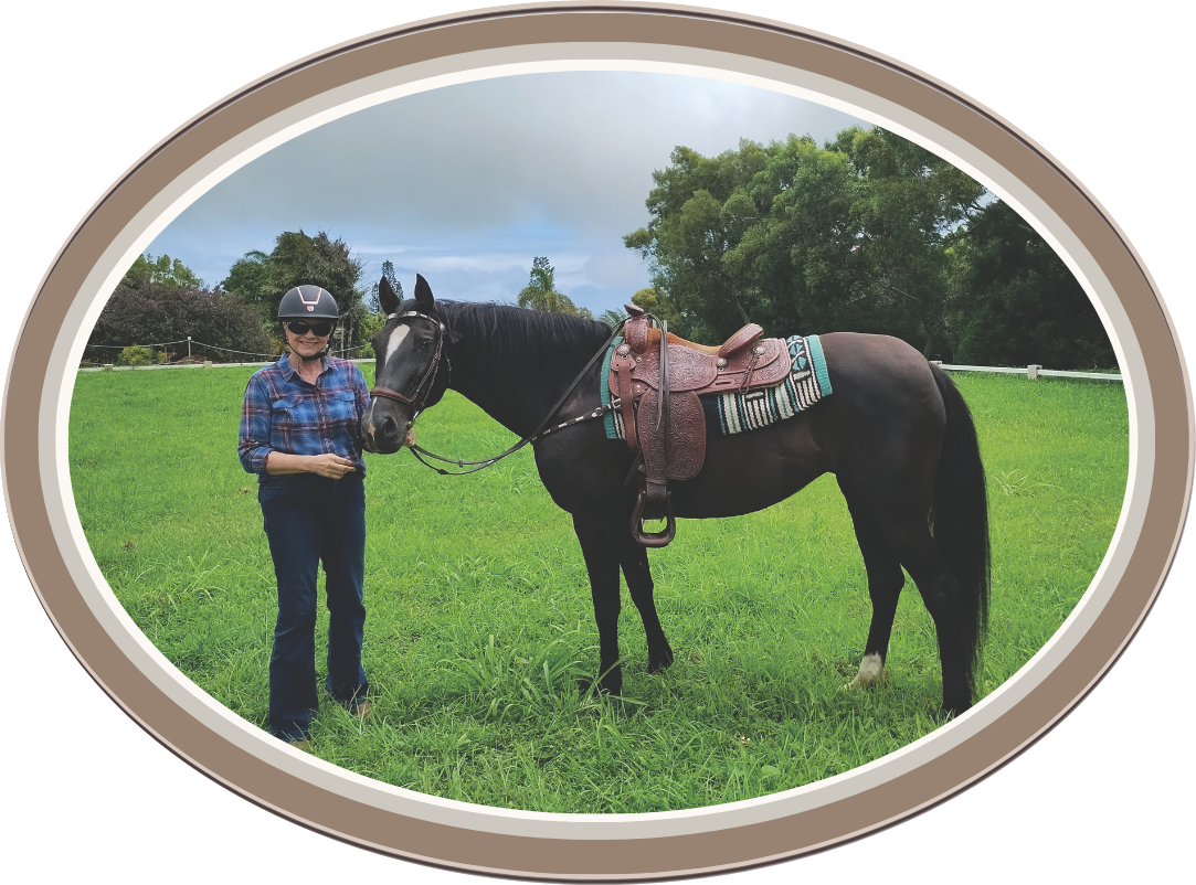Linda Anne Starr in a plaid shirt, jeans, and riding helmet standing next to a black horse with a saddle and a blanket in a grassy field with trees in the background. Linda Anne Starr | Training the Horse's Beautiful Mind