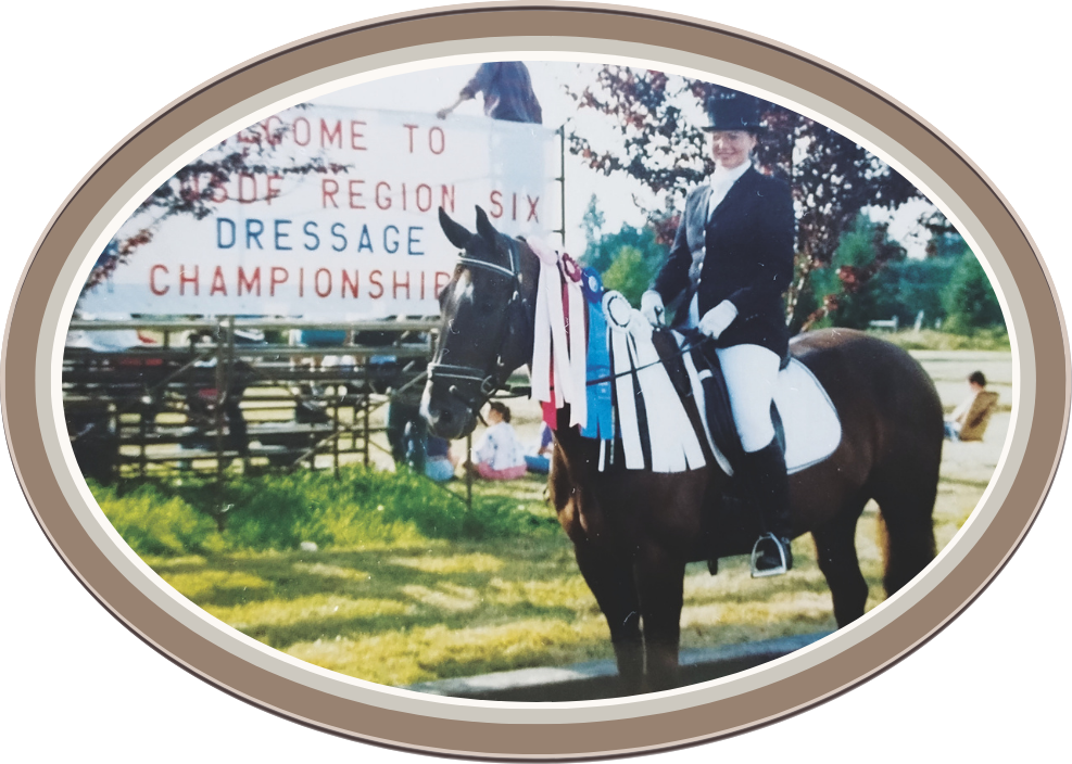 Linda Anne Starr in equestrian attire riding a horse with ribbons, standing in front of a sign that reads 'Welcome to Region Six Dressage Championship.' Linda Anne Starr | Training the Horse's Beautiful Mind