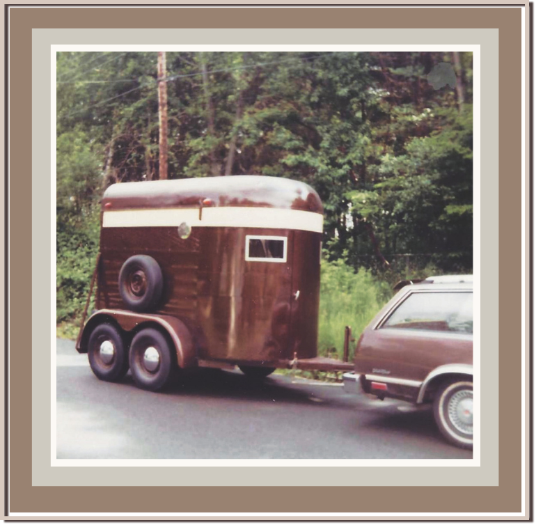 A vintage brown horse trailer hitched to a brown station wagon on a rural road with trees in the background. Linda Anne Starr | Training the Horse's Beautiful Mind