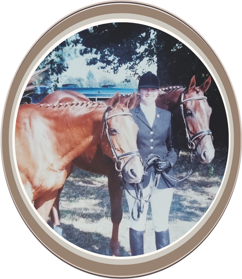 Linda Anne Starr dressed in equestrian attire standing outdoors, holding two brown horses with bridles, with trees and a trailer in the background. Linda Anne Starr | Training the Horse's Beautiful Mind