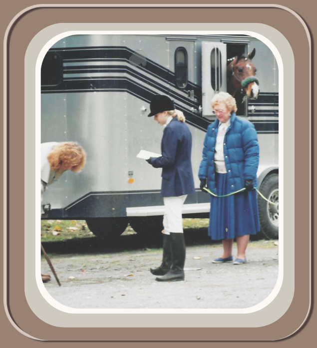 Three women and a horse peeking out of a horse trailer, with one woman reading a notebook and another holding a leash, on a gravel surface with fallen leaves. Linda Anne Starr | Training the Horse's Beautiful Mind