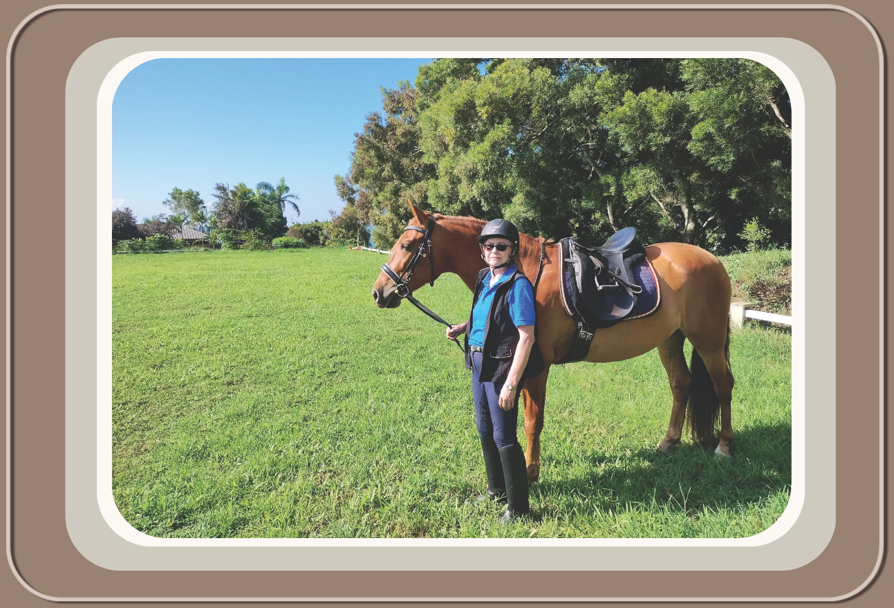 Linda Anne Starr with sunglasses and a helmet standing next to a brown horse on a grassy field with trees in the background. Linda Anne Starr | Training the Horse's Beautiful Mind