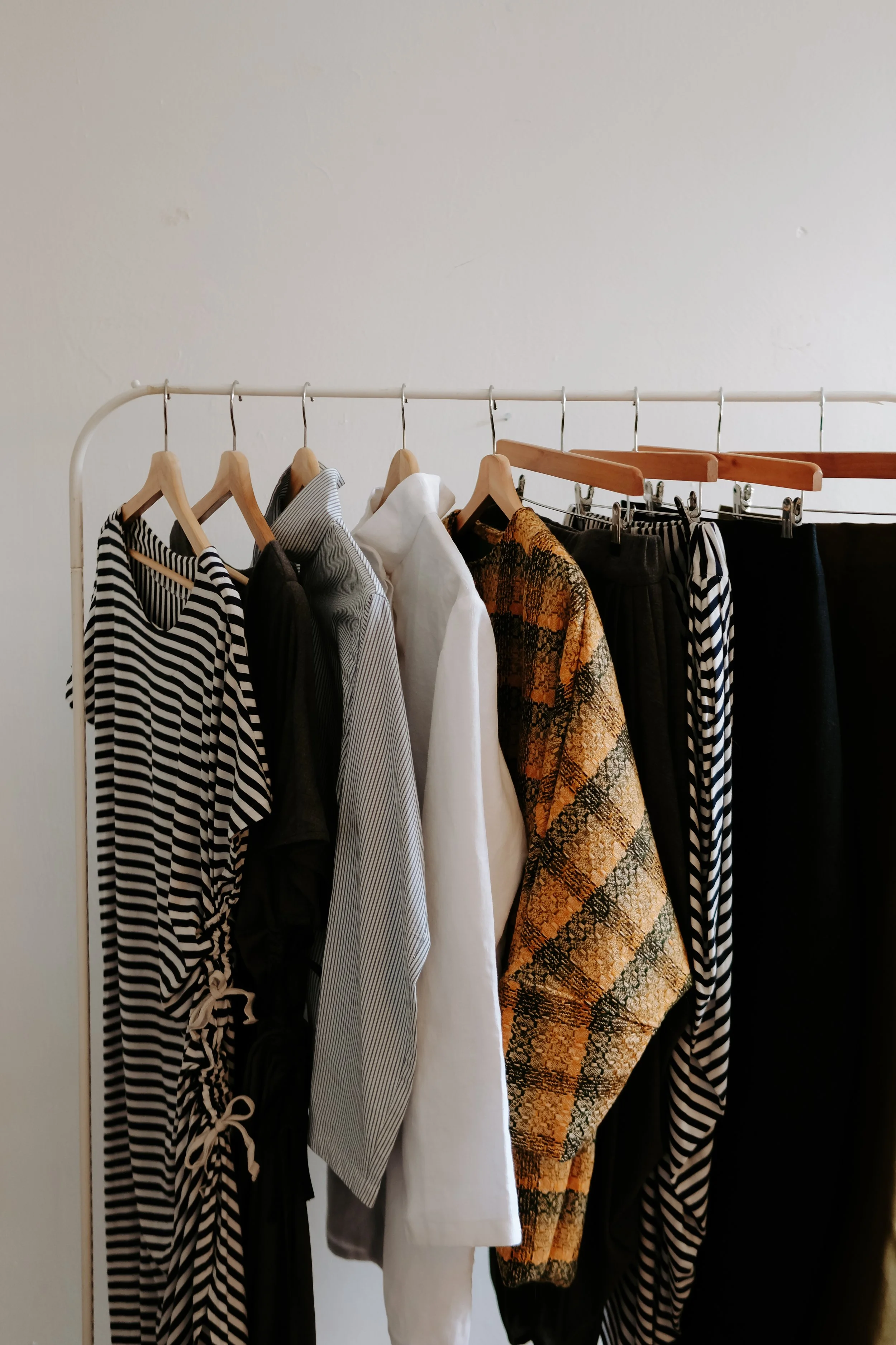 Clothes hanging on a white clothing rack, including striped, black, white, patterned, and solid-colored garments.
