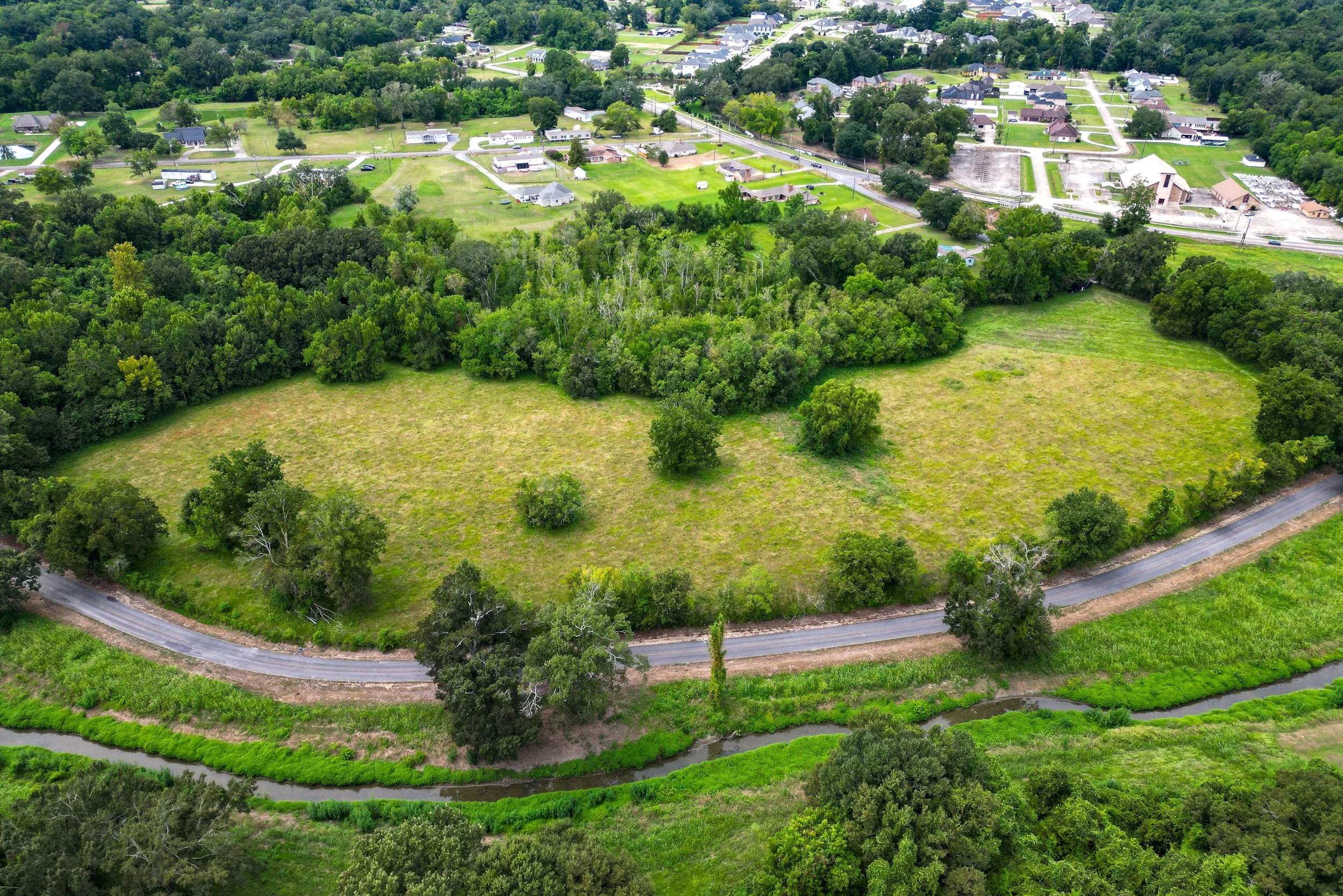 Aerial view of a suburban neighborhood with green trees, houses, and a winding road.