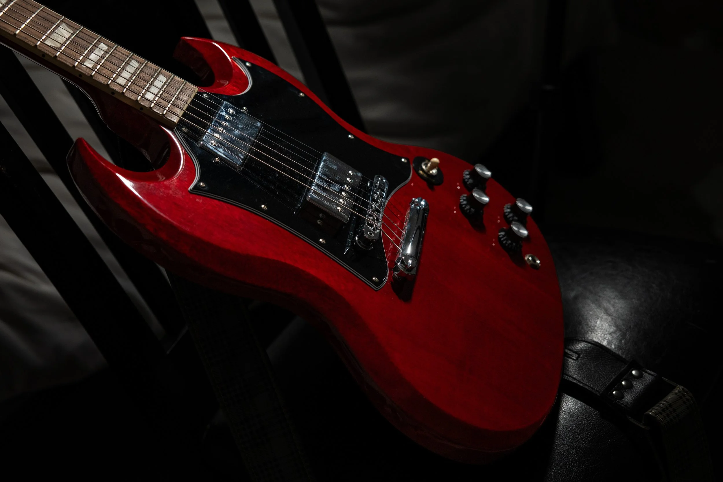 A red electric guitar resting on a dark surface with black slats in the background.