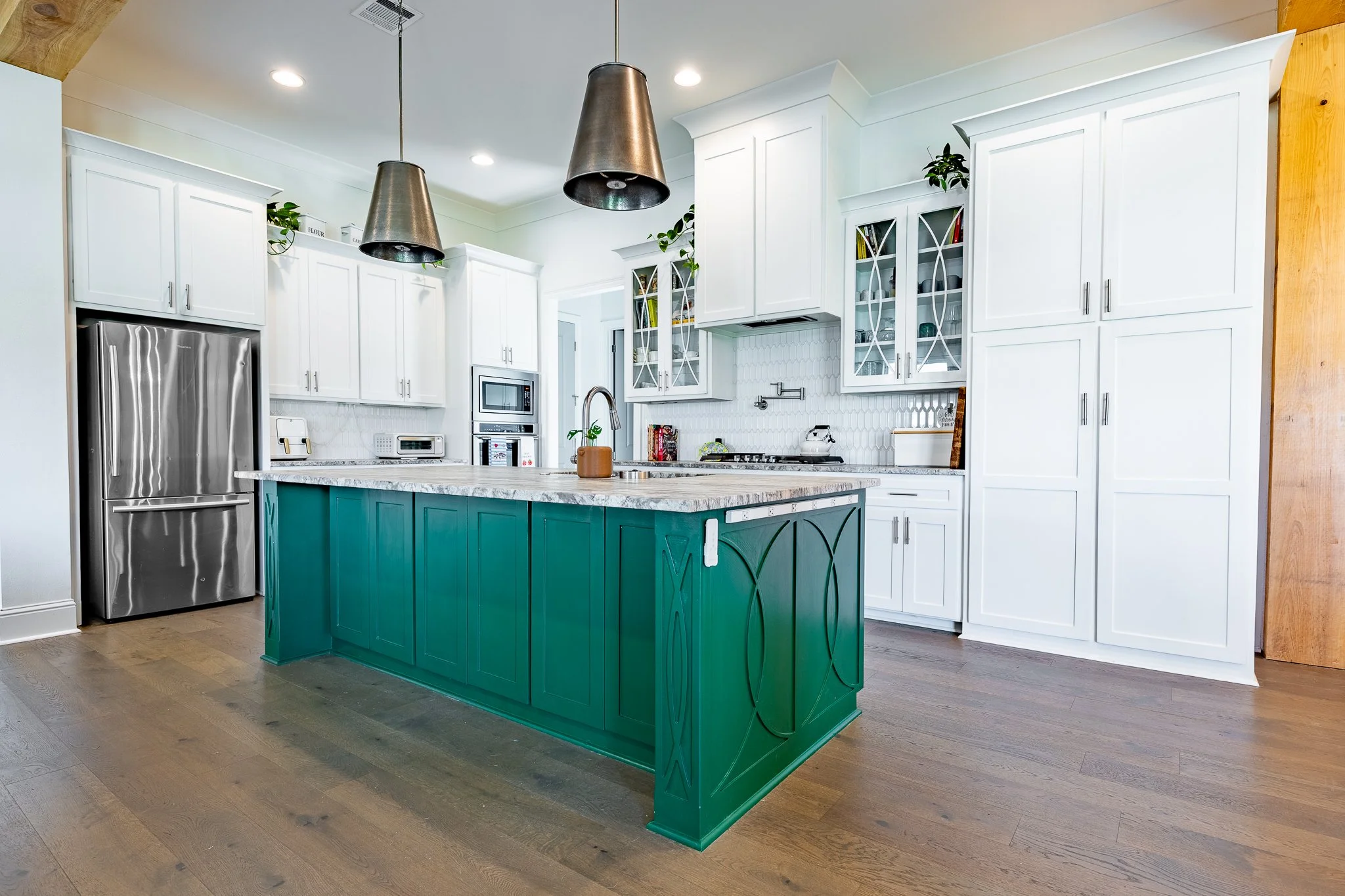 Modern kitchen with white cabinets, a teal island, stainless steel refrigerator, and pendant lights.