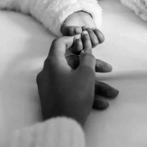 A close-up of an adult's hand gently holding a baby's hand.