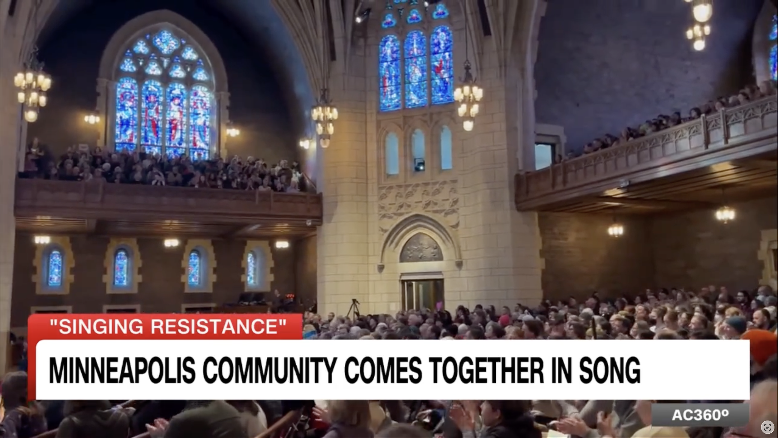 Inside a church with stained glass windows and a large congregation, the scene shows numerous people seated and standing in the pews, focusing on a community singing event. The caption indicates the event is titled 'Singing Resistance' and involves a Minneapolis community coming together in song.