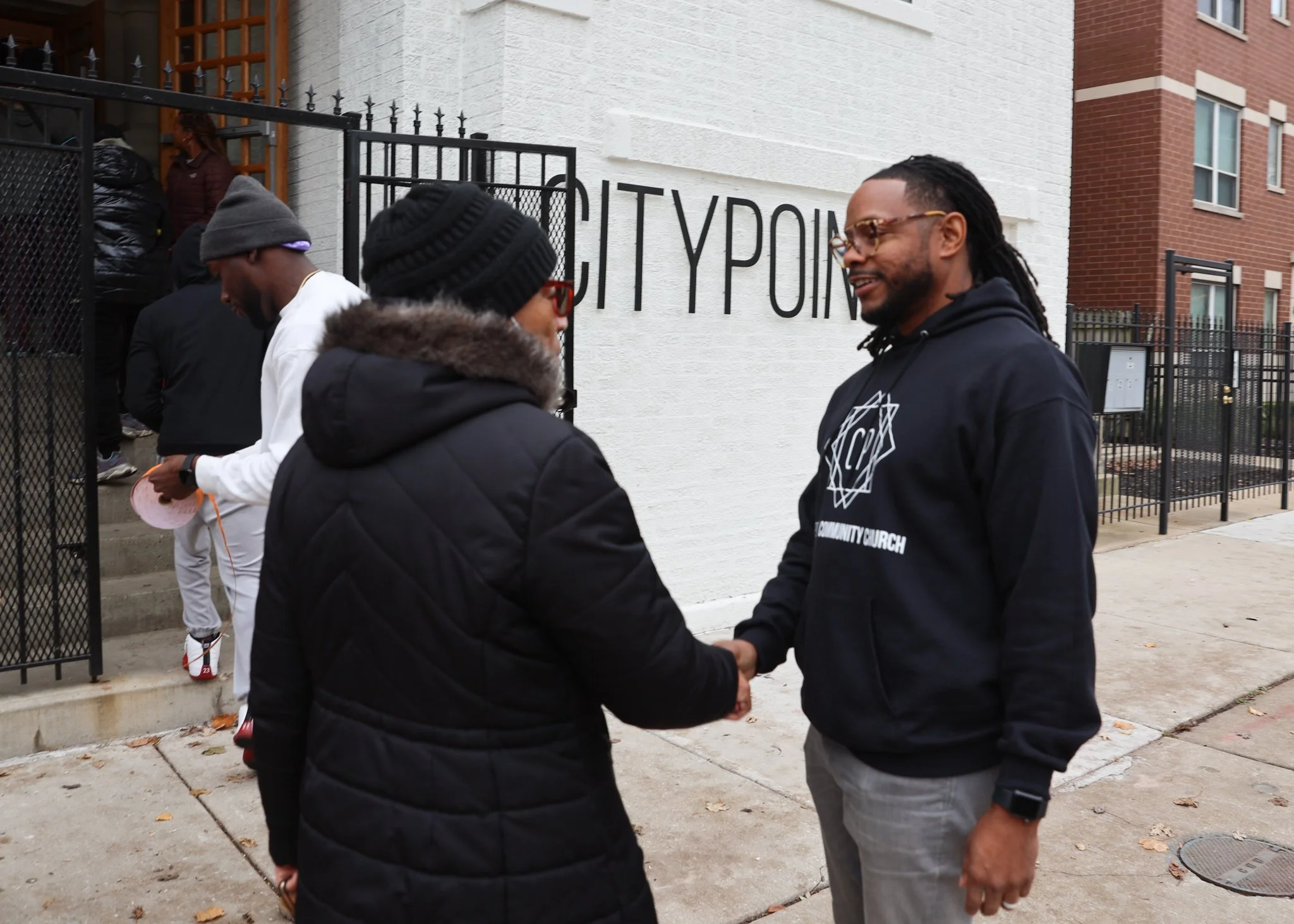 Two people shaking hands outside near a building with a sign reading 'CITY P...