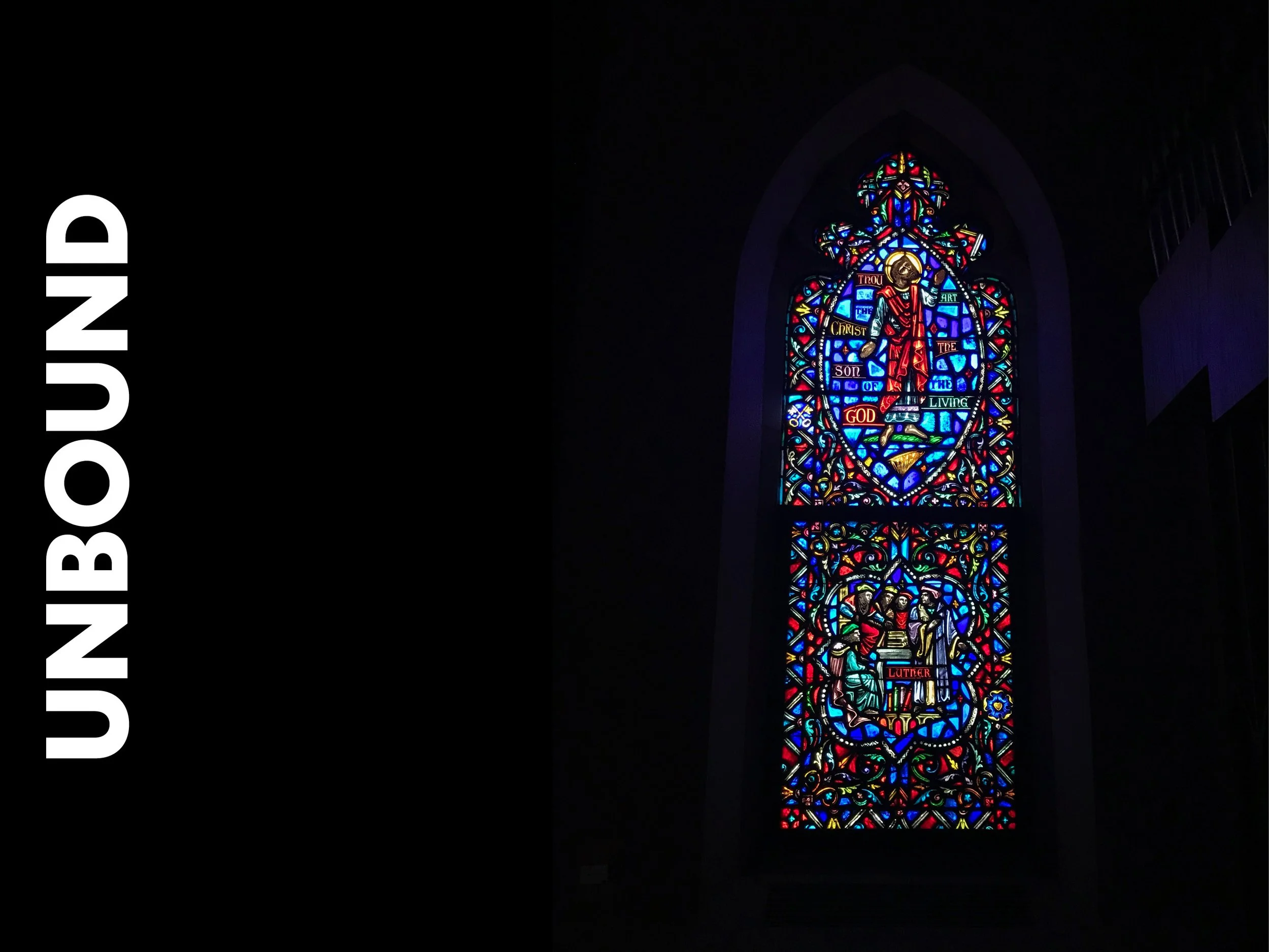 Colorful stained glass window depicting religious figures and symbols, with the words 'through the Christ the Son of God living Luther' at the bottom.